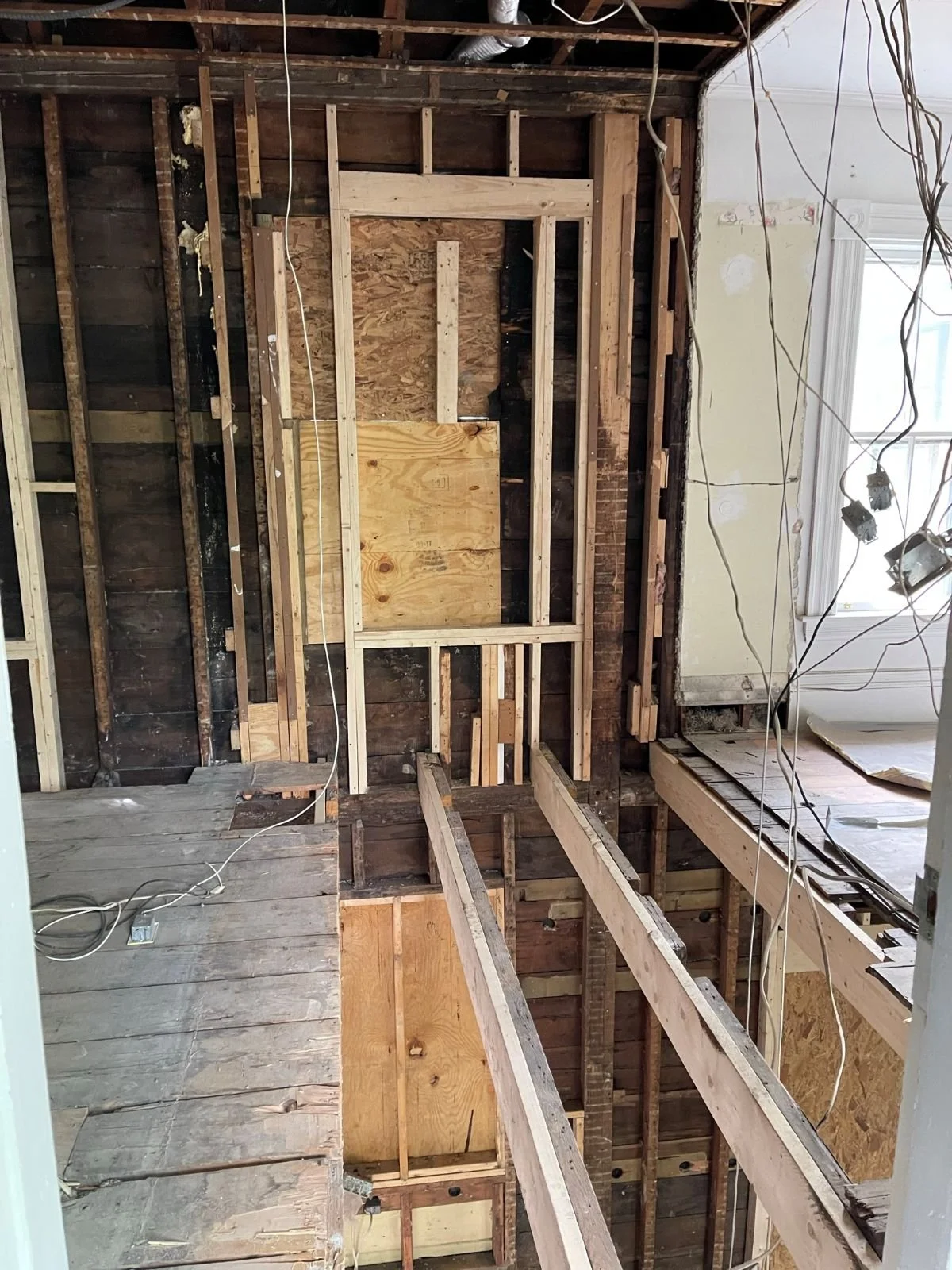 Construction phase of kids bath and laundry reconfiguration in an 1846 Victorian home in Newton MA showing chimney removal, new window framing and joist sistering during renovation