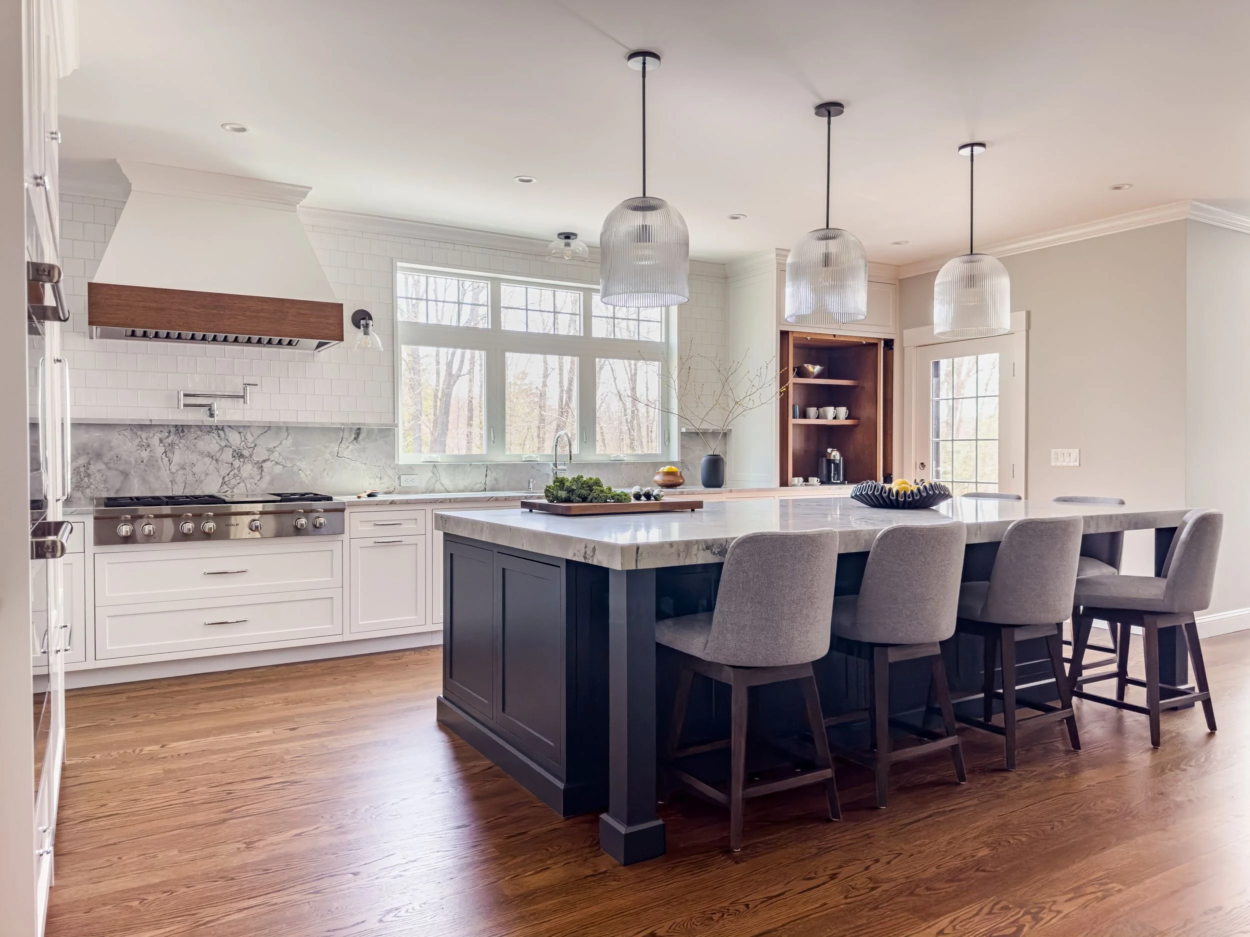 Open-concept kitchen addition with large island painted in Benjamin Moore Blue Note, fluted glass pendant lights, natural stone quartzite countertops, Wolf professional range, super white quartzite slab backsplash and custom cabinet in Hamilton, MA