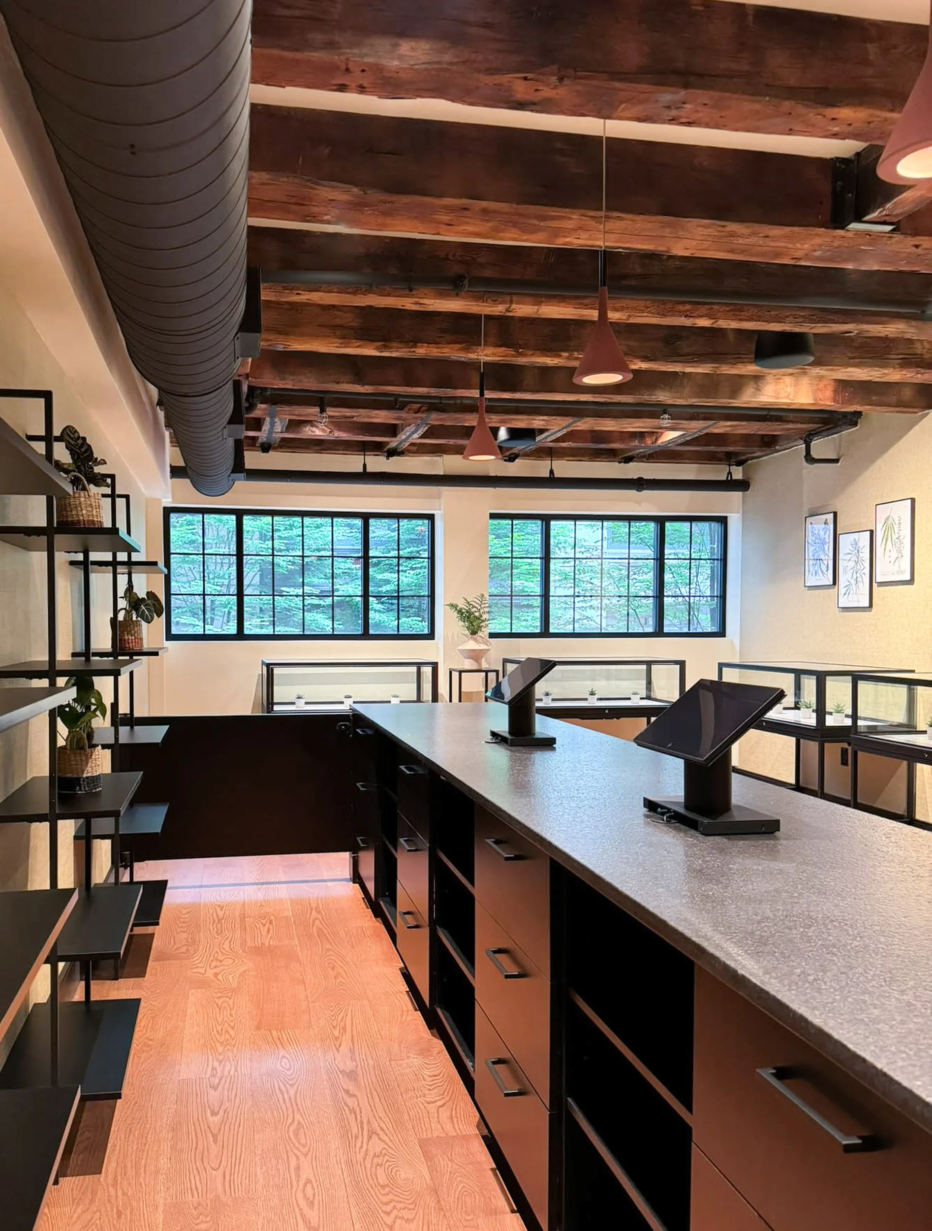 Retail custom cash wrap with drawers and open shelving for equipment and storage with black displays beyond and large horizontal windows under original heavy timber beams.