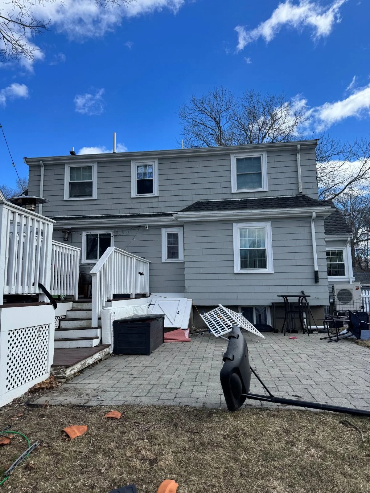 Existing conditions of the rear of a colonial home in Melrose, MA prior to kitchen addition, showing original deck, patio, and back entrance before renovation.