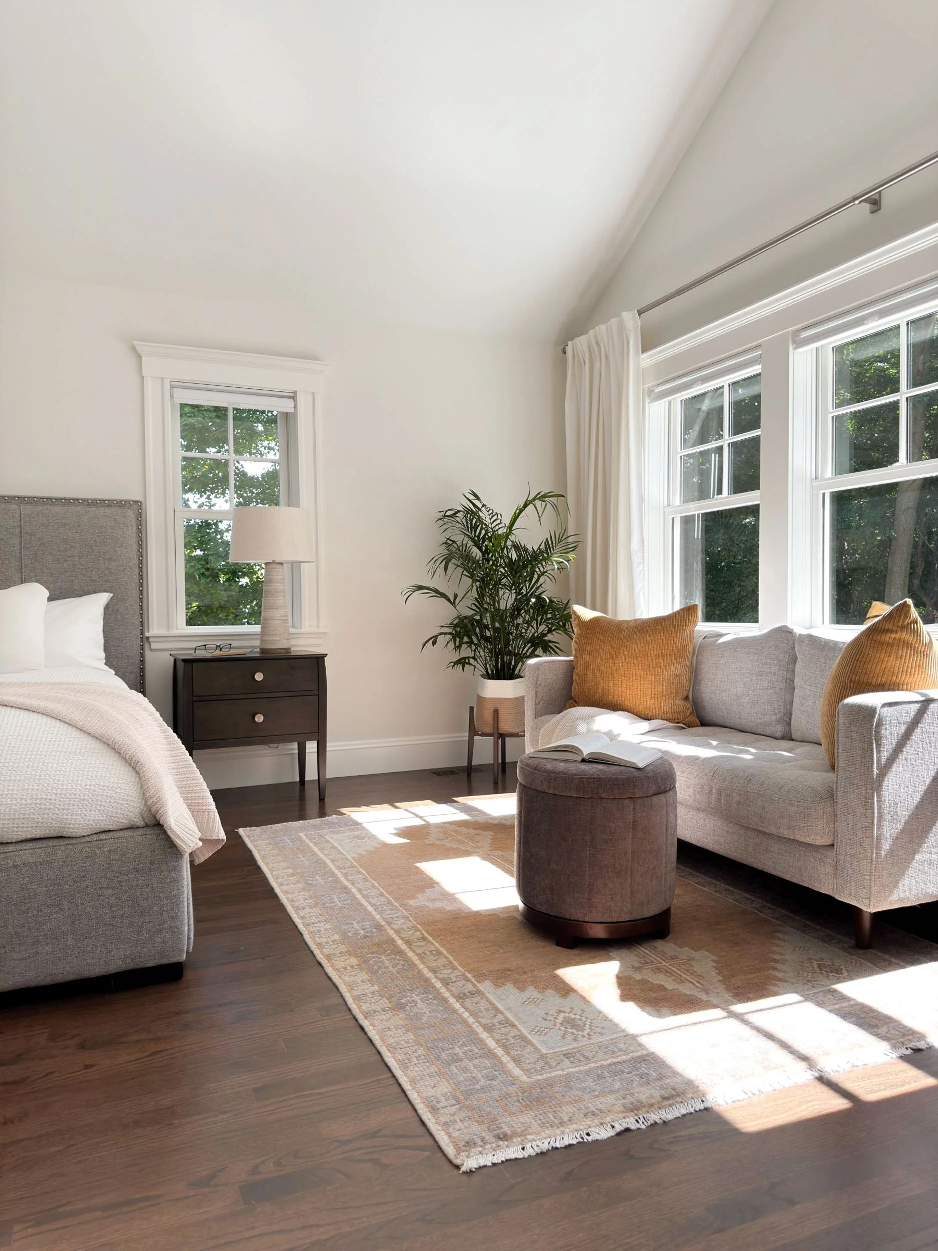 Completed primary suite bedroom of a Dutch Colonial second story addition in Greater Boston showing reading area, vaulted ceiling and triple window array with natural light.