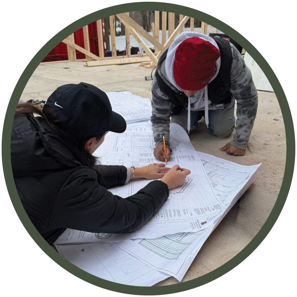 Architect Olivia Dube on-site reviewing large-format framing plans for a two-story addition with a contractor to coordinate design intent with existing conditions.