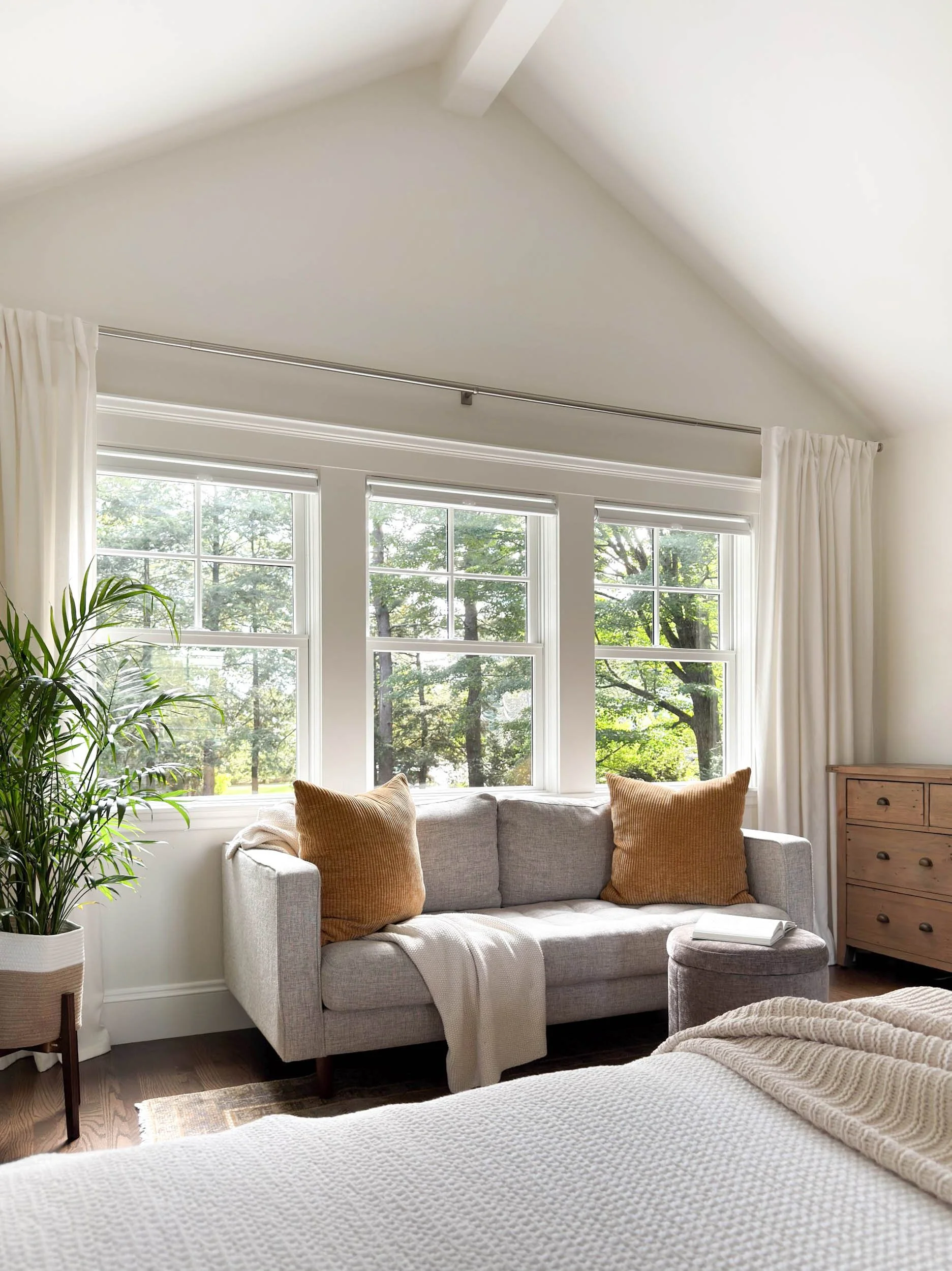 Interior of new vaulted primary suite in second story addition featuring triple window overlooking lush backyard and sofa reading area.