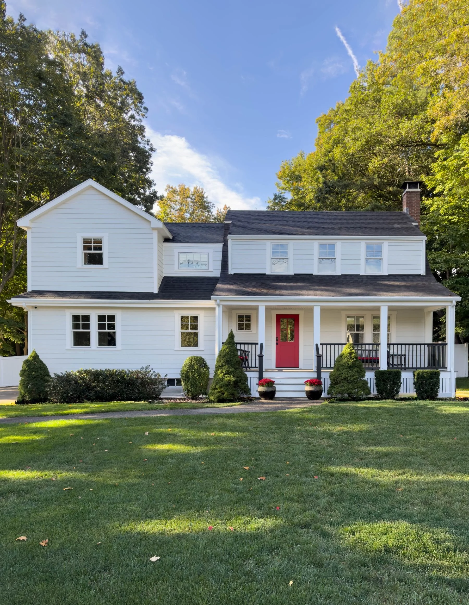 Completed front exterior of a Dutch Colonial second story addition in Greater Boston showing finished Hardie siding, Marvin windows, covered porch and red entry door designed by Tact and Grit Design Co.