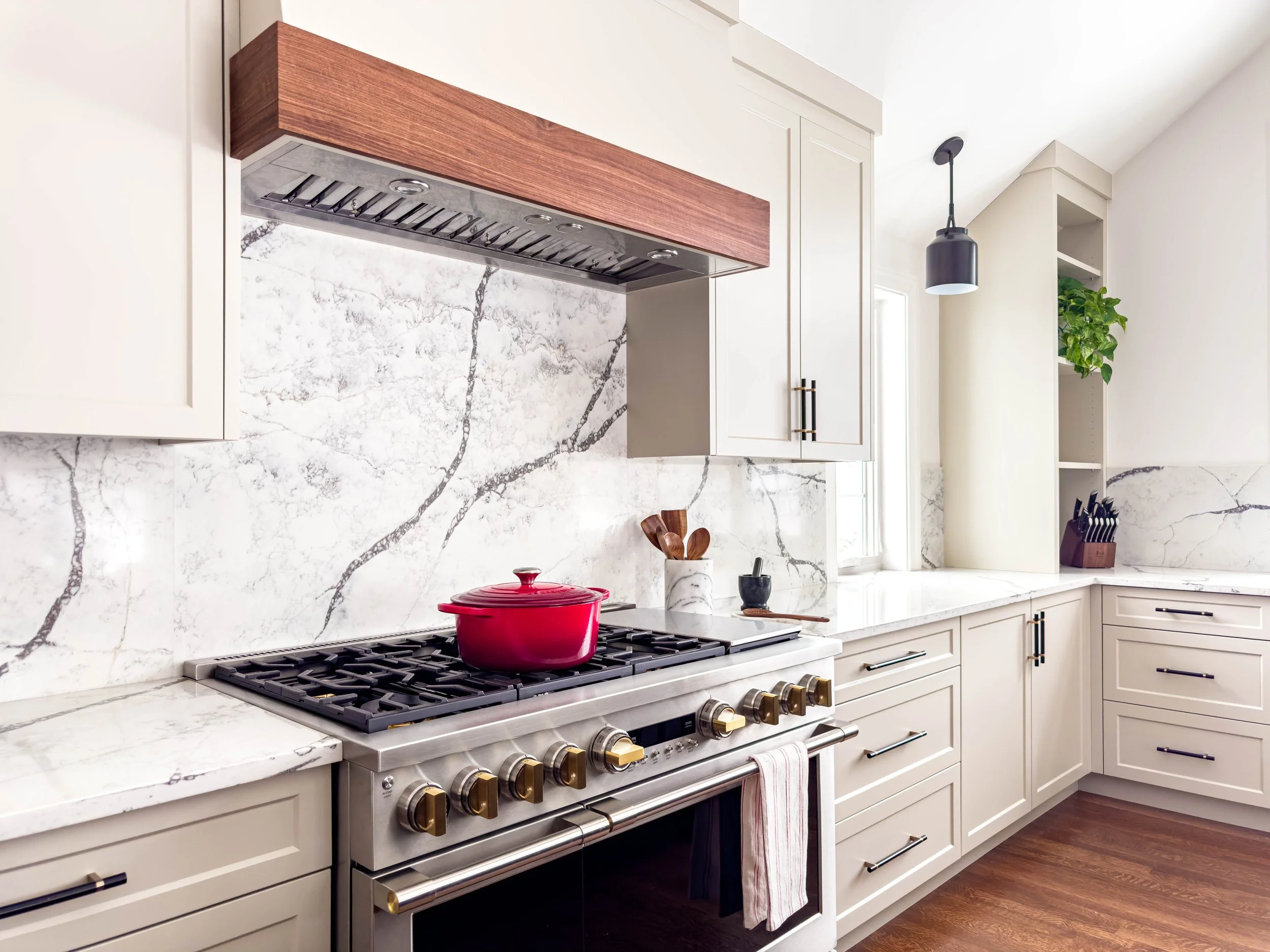 Professional kitchen workstation featuring a 48" Monogram 6-burner range with a custom walnut-trimmed vent hood and a full-height marble-style quartz backsplash.