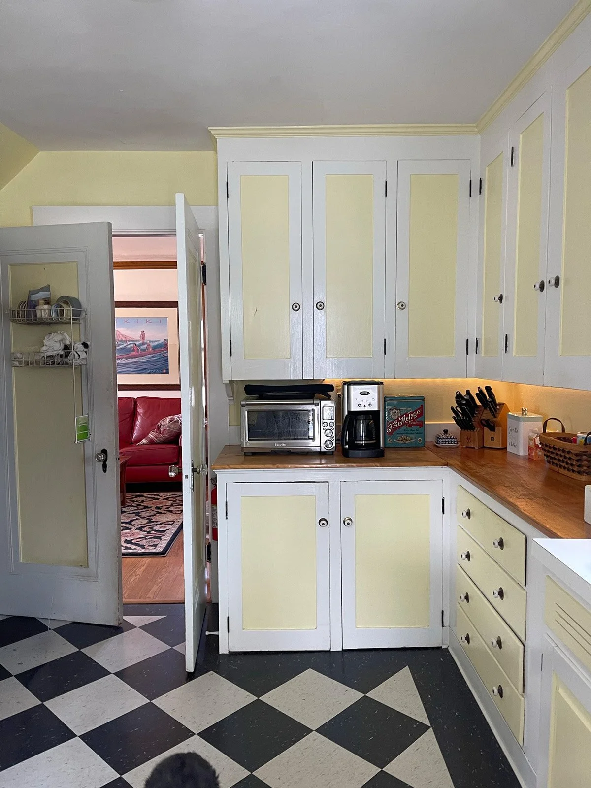 Existing two toned kitchen corner cabinetry with butcher block countertops and view to living room with open door to basement