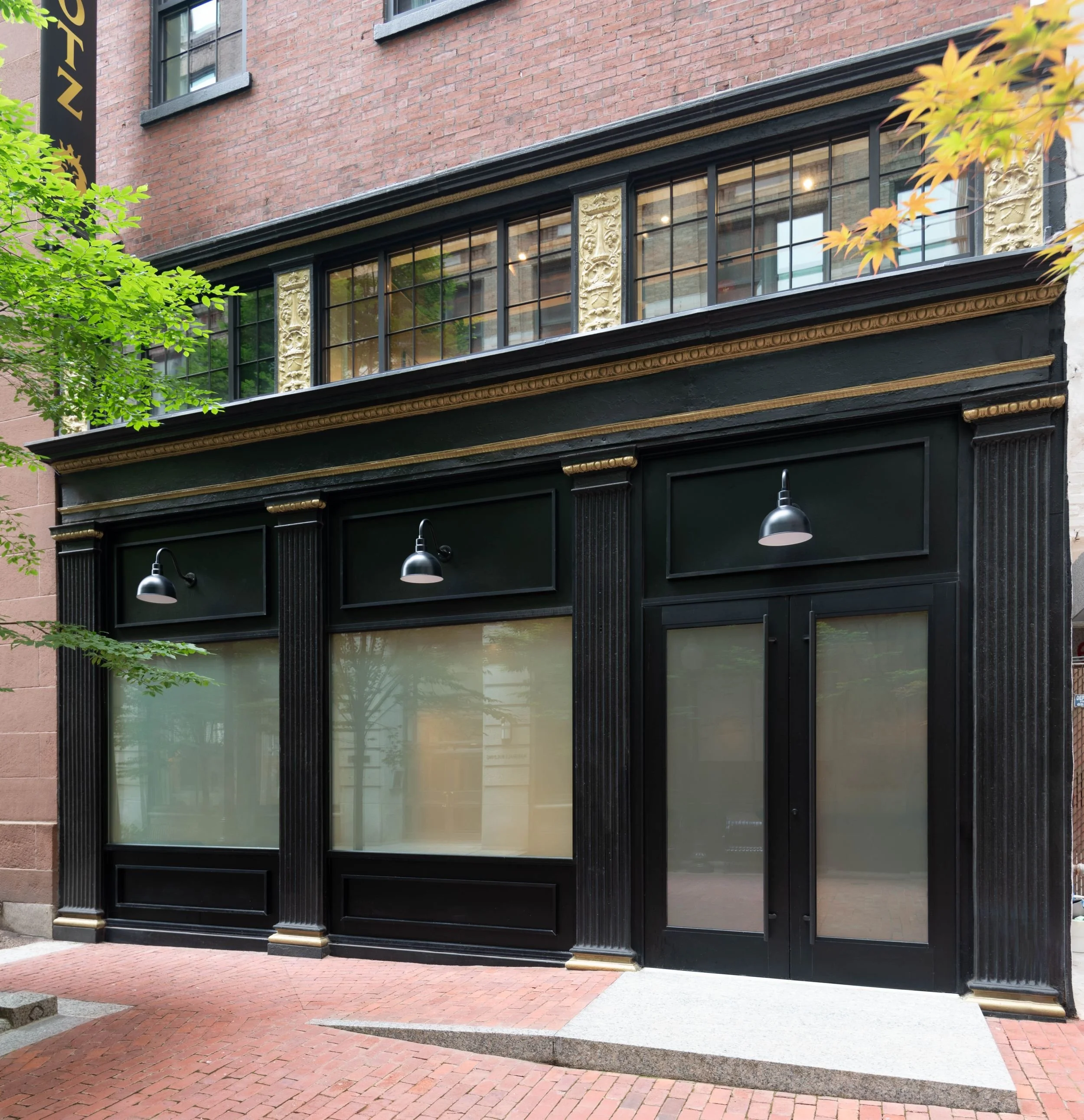 Black and gold storefront with ornate cast iron facade with black gooseneck light fixtures