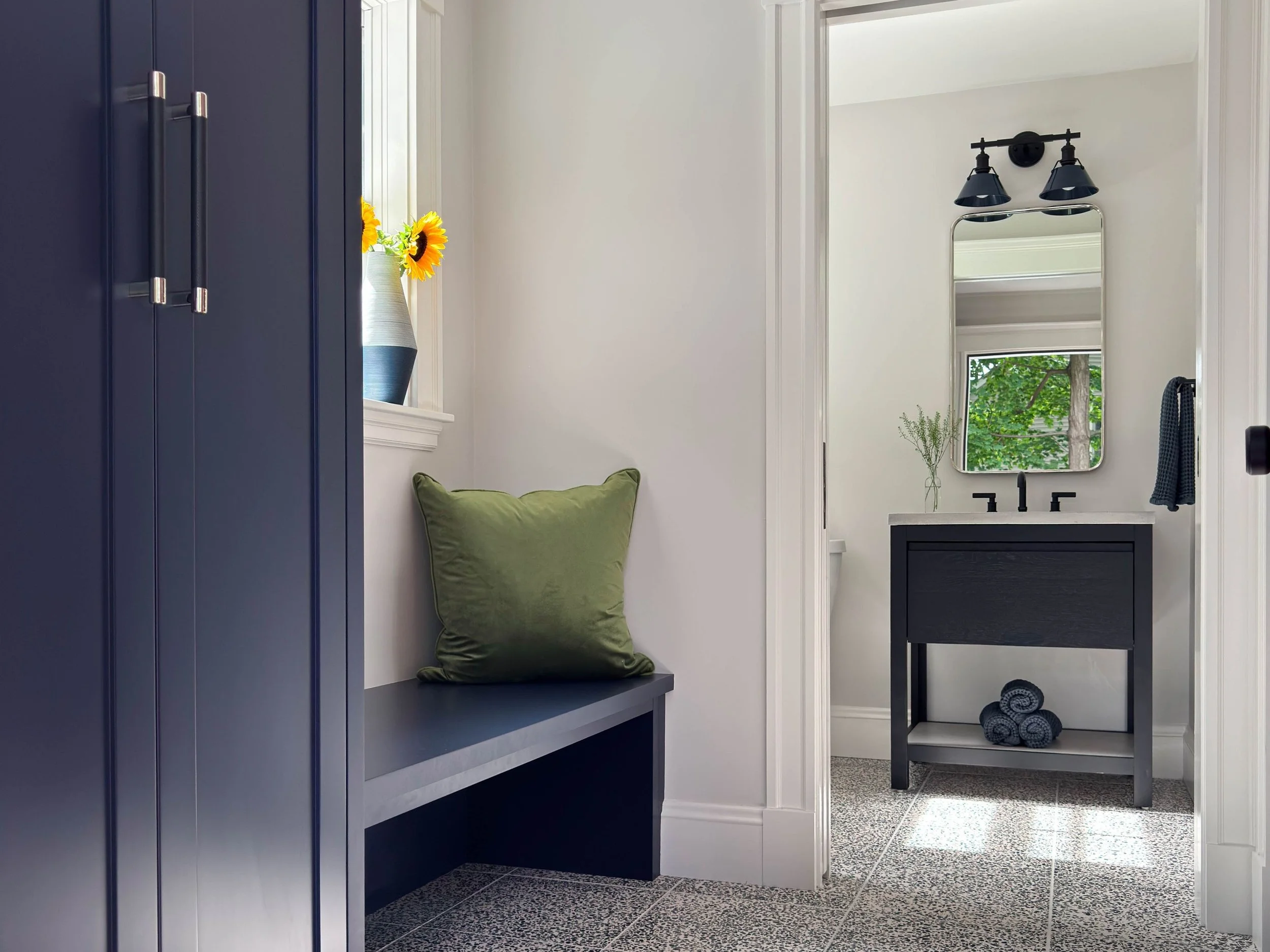 Newly added mudroom with custom deep royal blue cabinetry and bench with view into powder room showcasing a black stained oak vanity with concrete countertop and blue light fixture