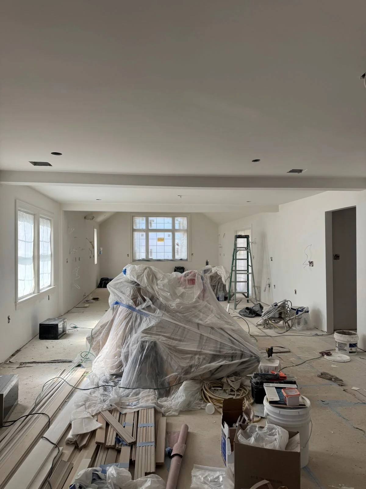 The unified living, dining, and kitchen areas freshly drywalled with new Marvin windows installed