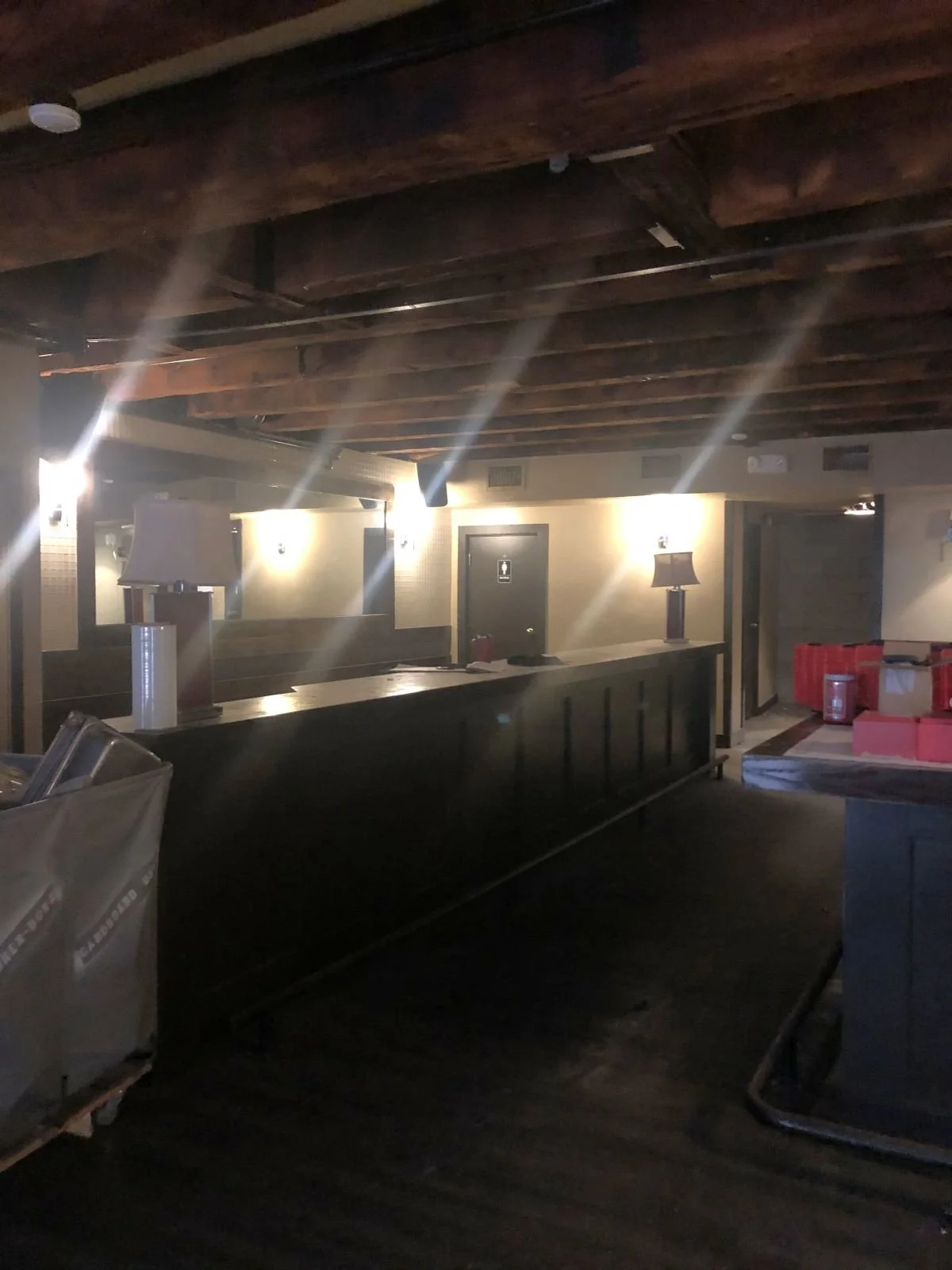 A dim bar standing area with exposed wood beams leading past a service counter