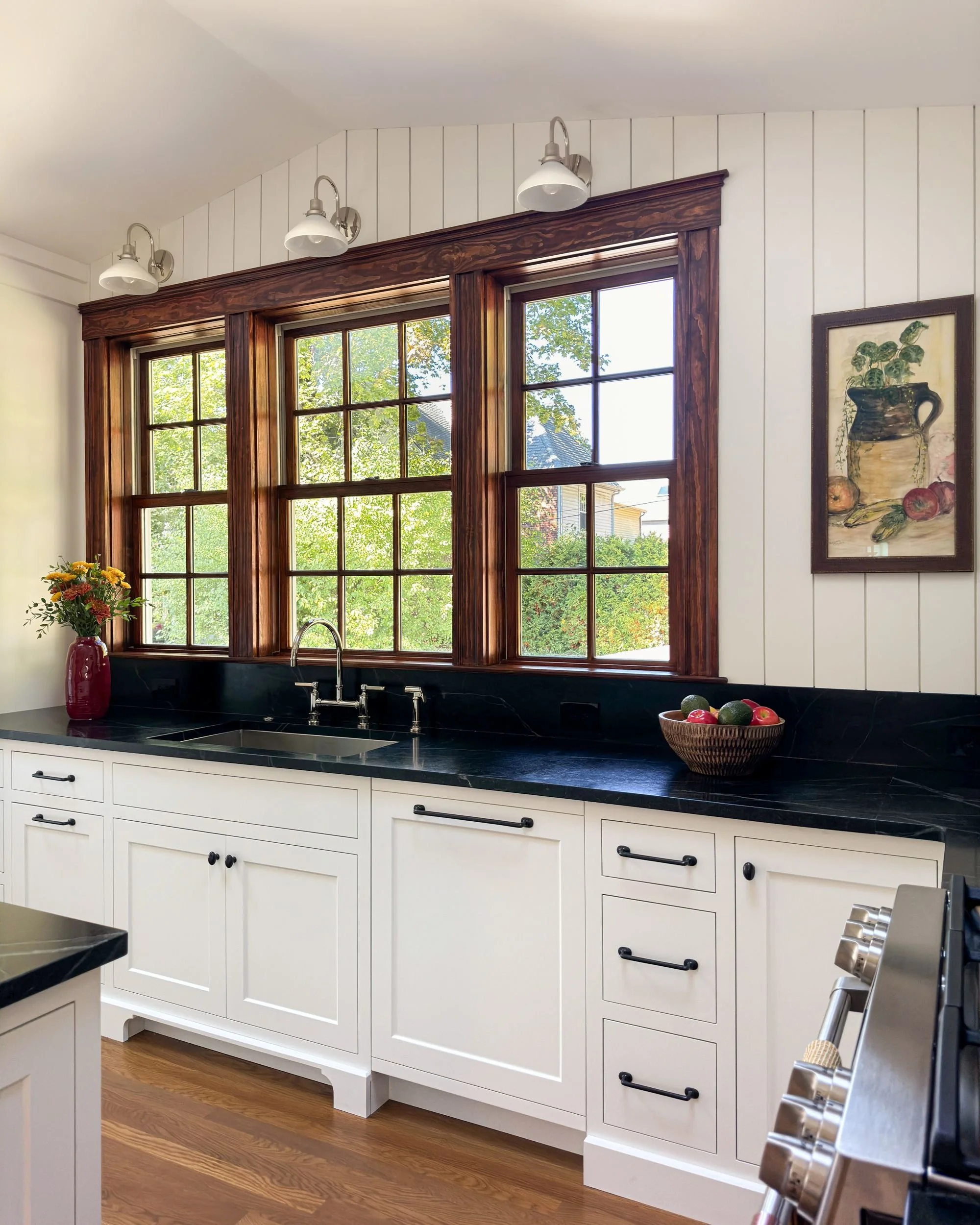 Alt: Sink wall with soapstone countertops, white shaker inset cabinetry, and triple wood-framed window overlooking the backyard, Medford MA kitchen addition