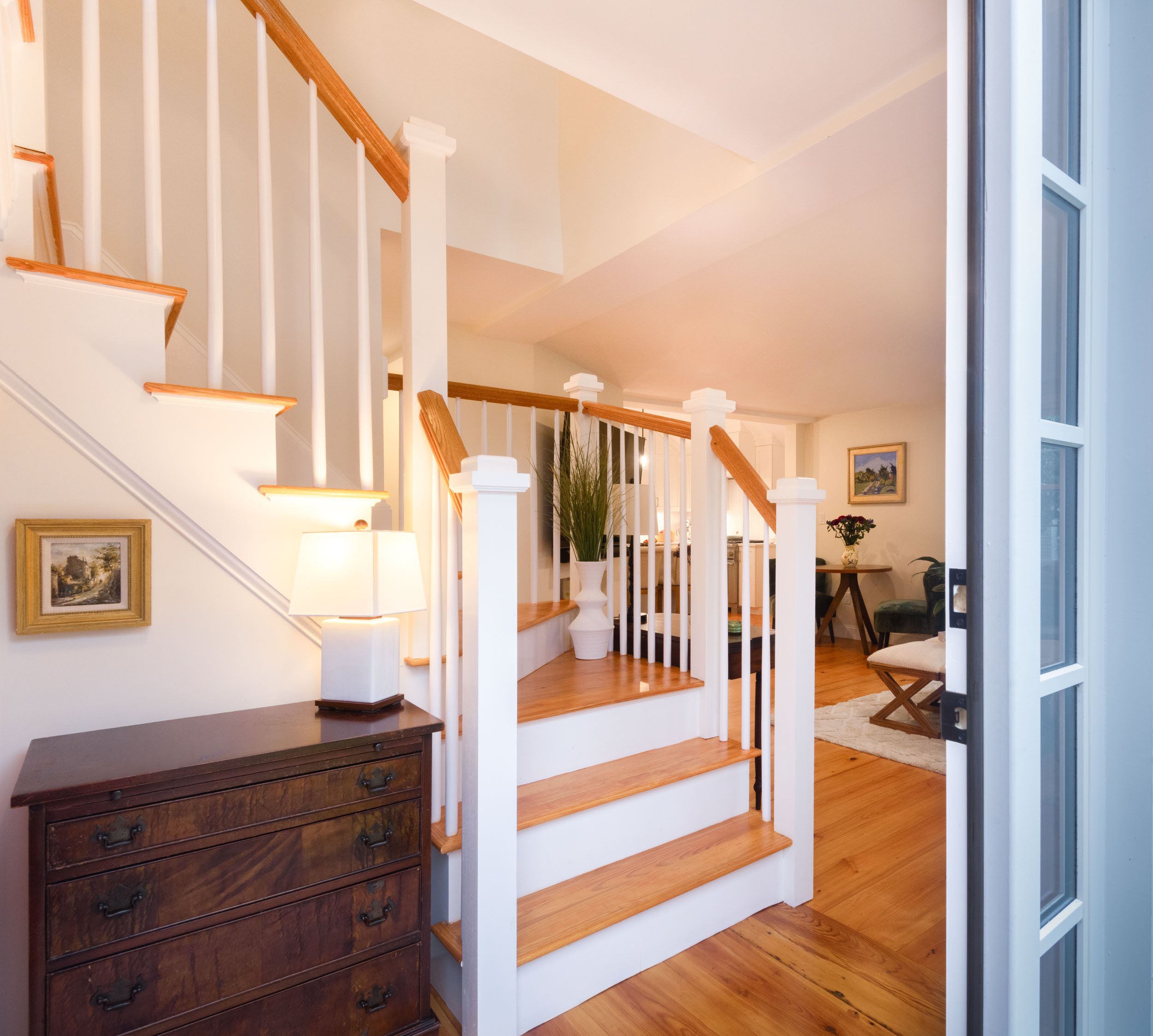 An entryway staircase open to the living room with wide plank pine flooring.