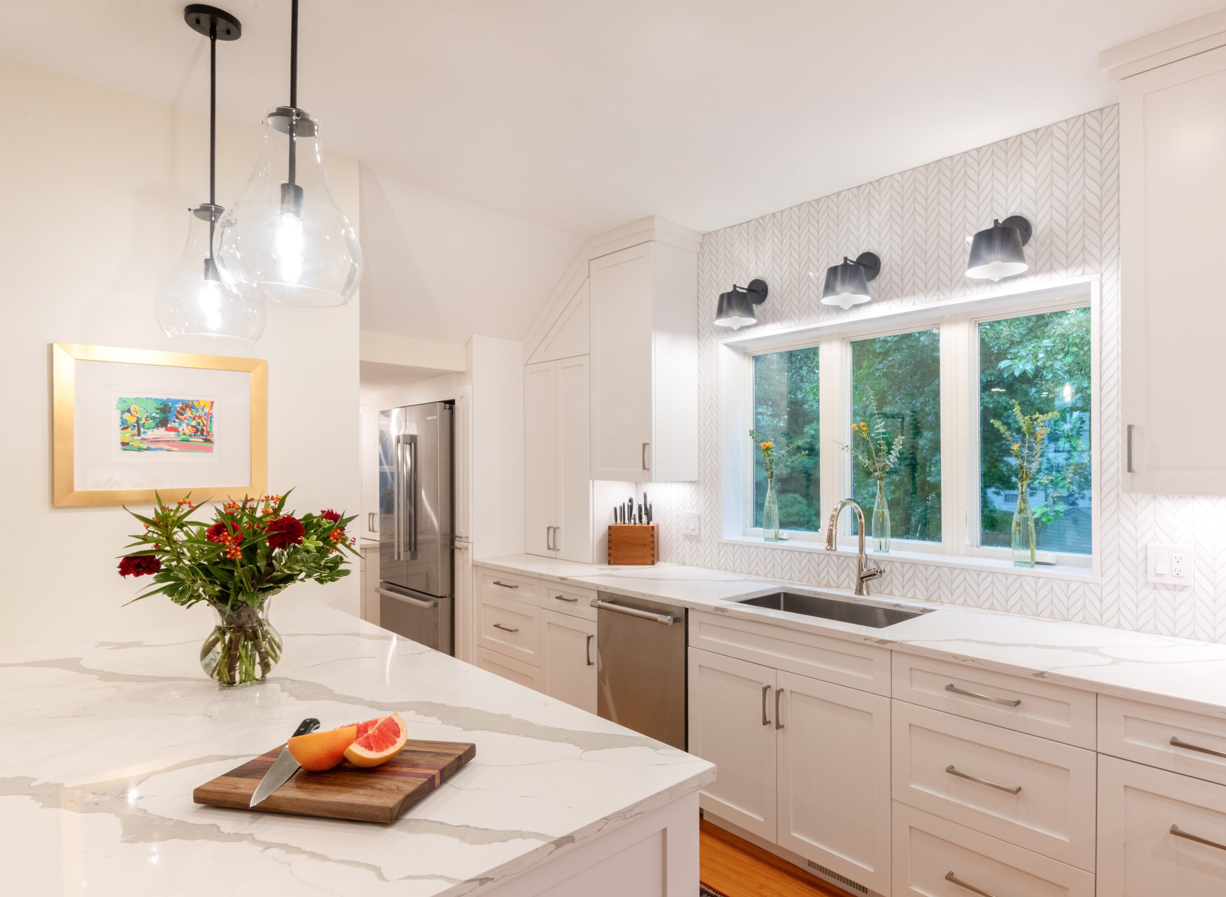 A kitchen island with view to a triple window at sink with sconces above.