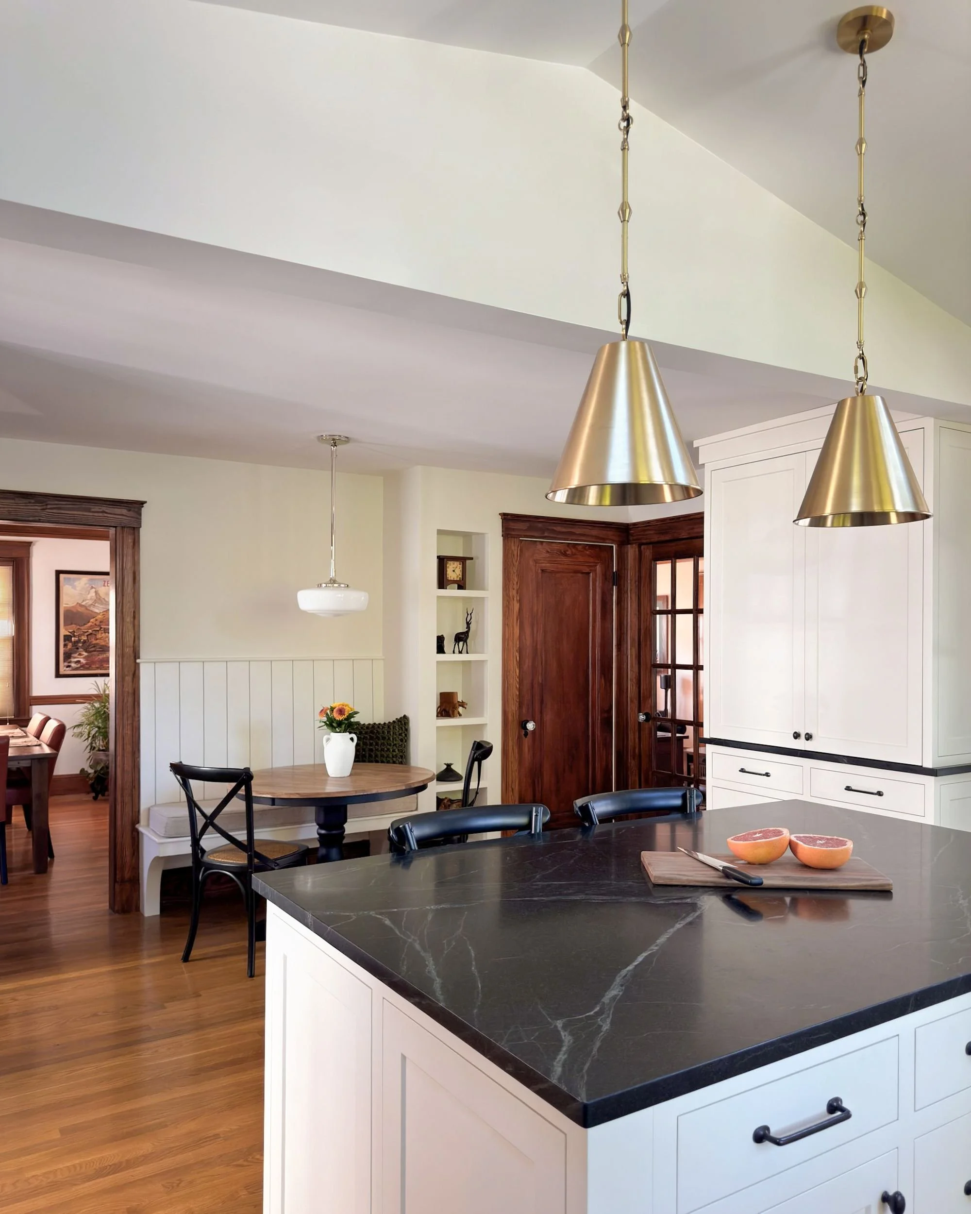 Soapstone island with brass pendant lighting overlooking breakfast nook with stained wood trim and built-in shelving, Medford MA kitchen addition