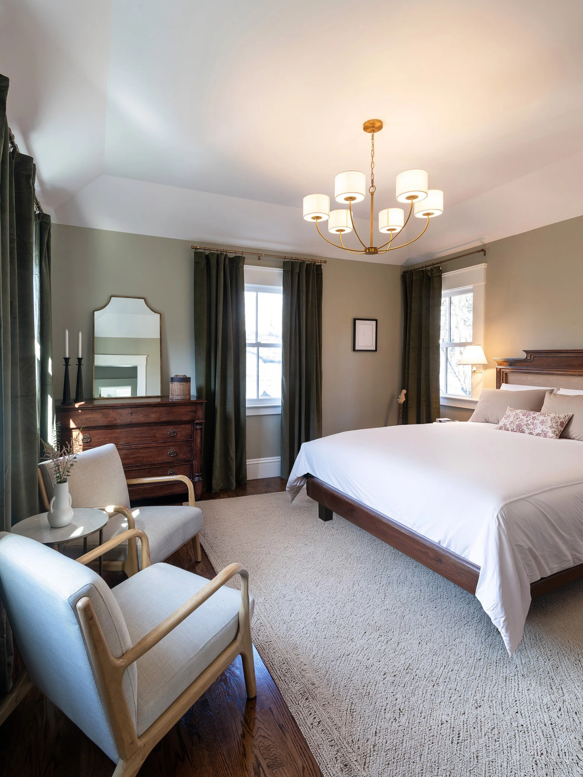 Renovated primary bedroom of an 1846 Victorian home in Newton MA featuring queen bed, brass chandelier and seating area with hardwood floors