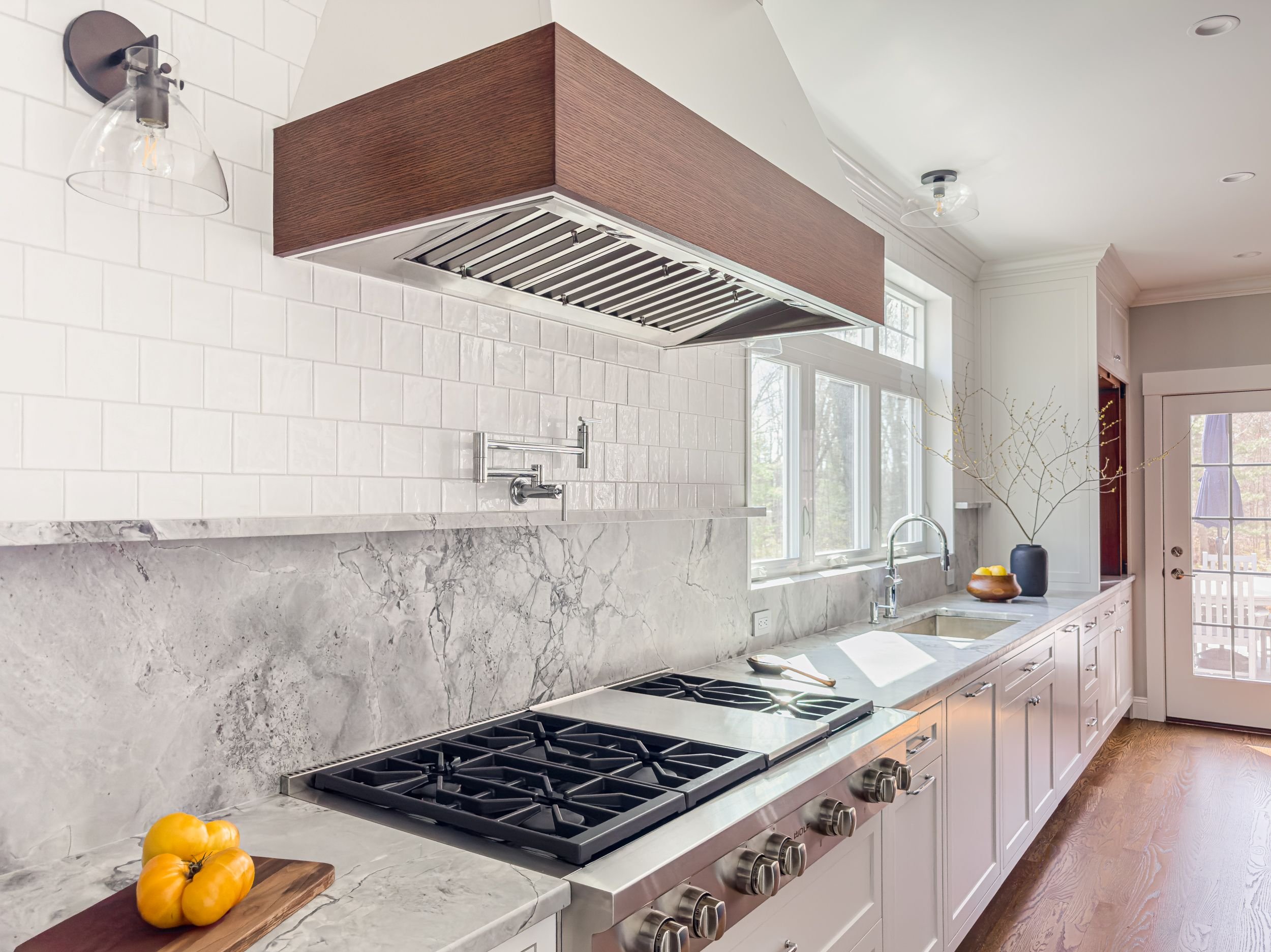 Wolf professional range with Super White quartzite slab backsplash, pot filler, walnut range hood, and white subway tile in Hamilton MA kitchen addition by Tact & Grit Design Co.