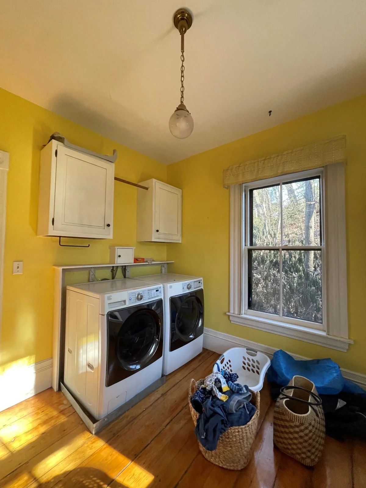 Existing laundry room of an 1846 Victorian home in Newton MA prior to renovation showing yellow painted walls and original hardwood floors before reconfiguration
