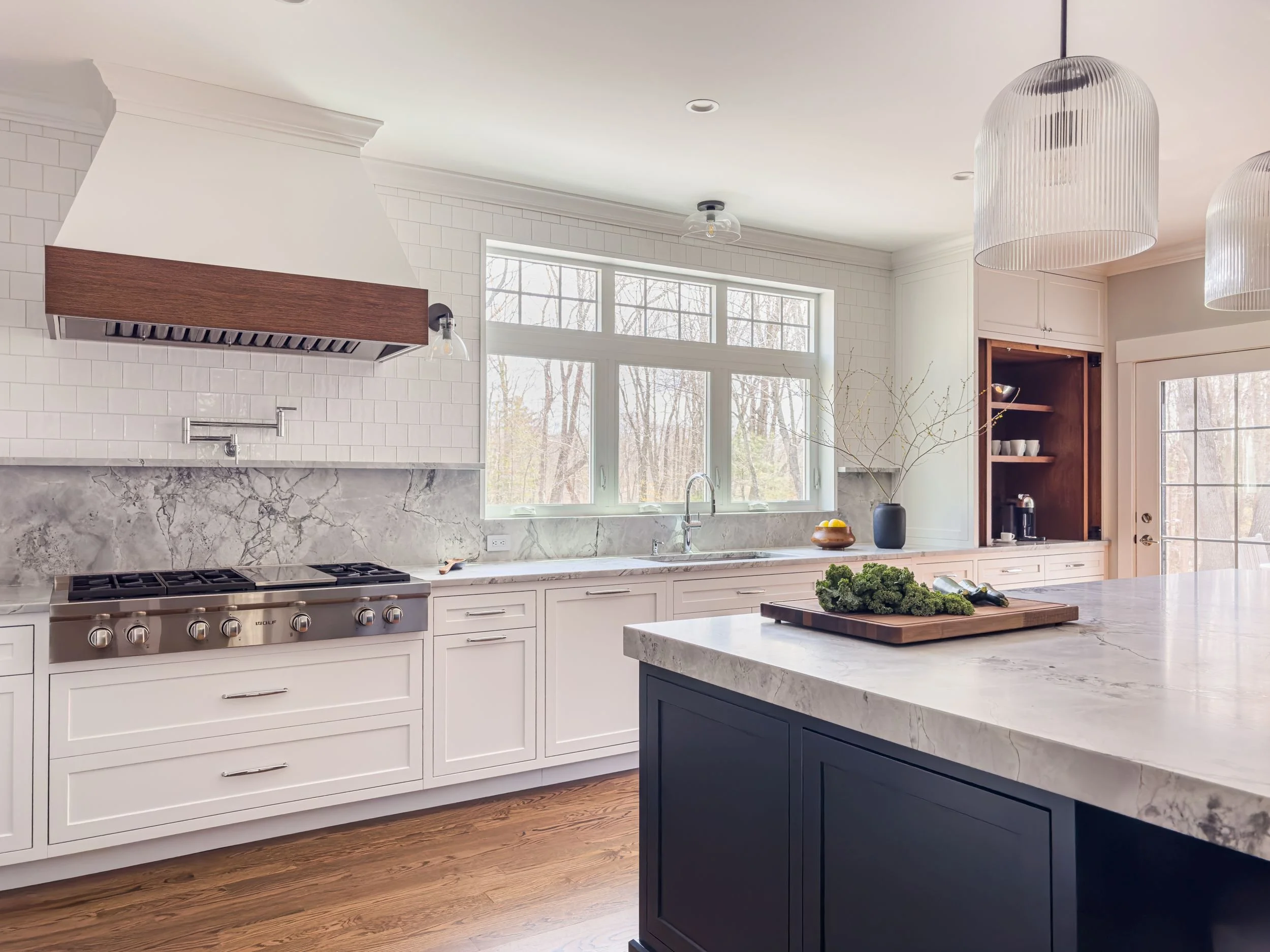Kitchen addition overview with walnut range hood, Super White quartzite backsplash, Wolf professional range, large Blue Note island, and fluted glass pendant light in Hamilton MA by Tact & Grit Design Co.