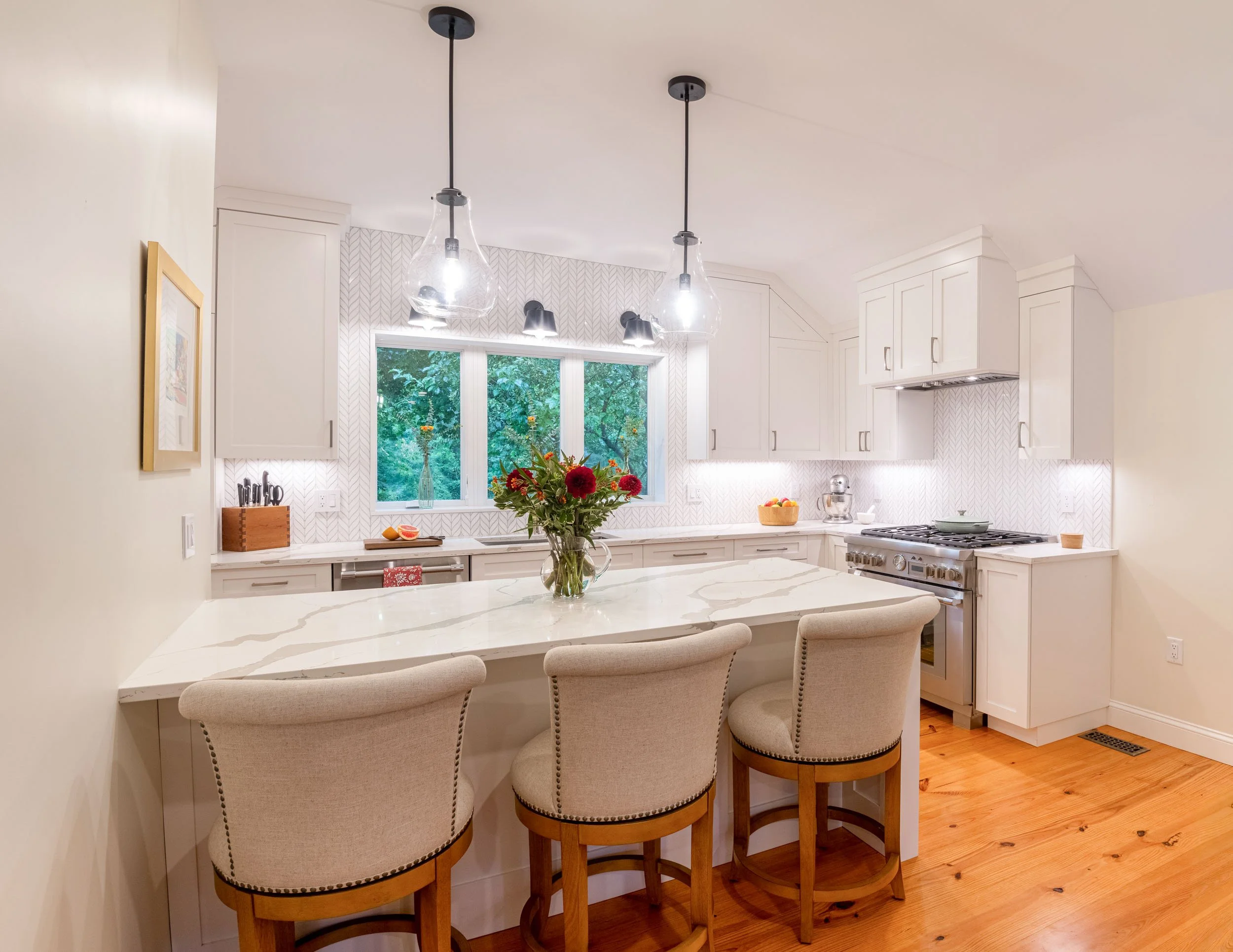 A kitchen island with pendant lighting and upholstered counter stools in a reconfigured Bedford Colonial.