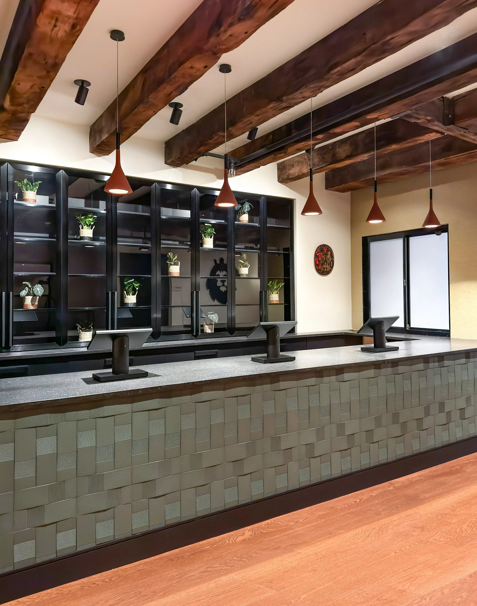 Green textured tile laid in a woven pattern at a custom POS with three registers, custom glass displays, heavy timber beams and red concrete lights with gold accent wall covering.