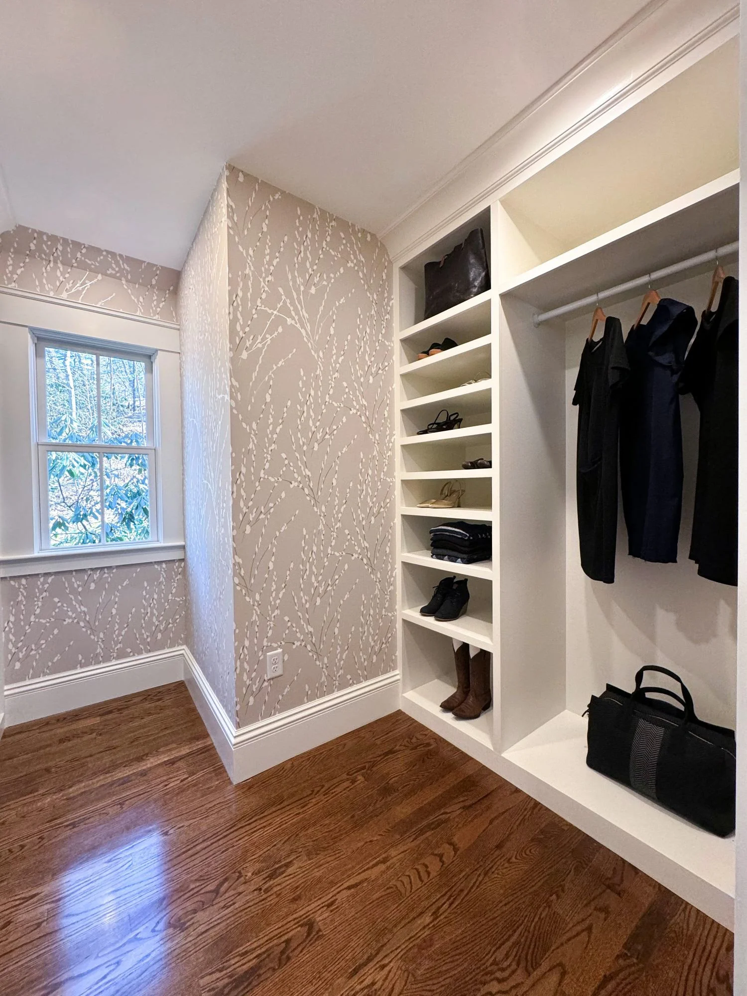 Renovated walk-in closet of an 1846 Victorian home in Newton MA featuring custom built-in shelving, shoe storage, hanging rods and decorative wallpaper