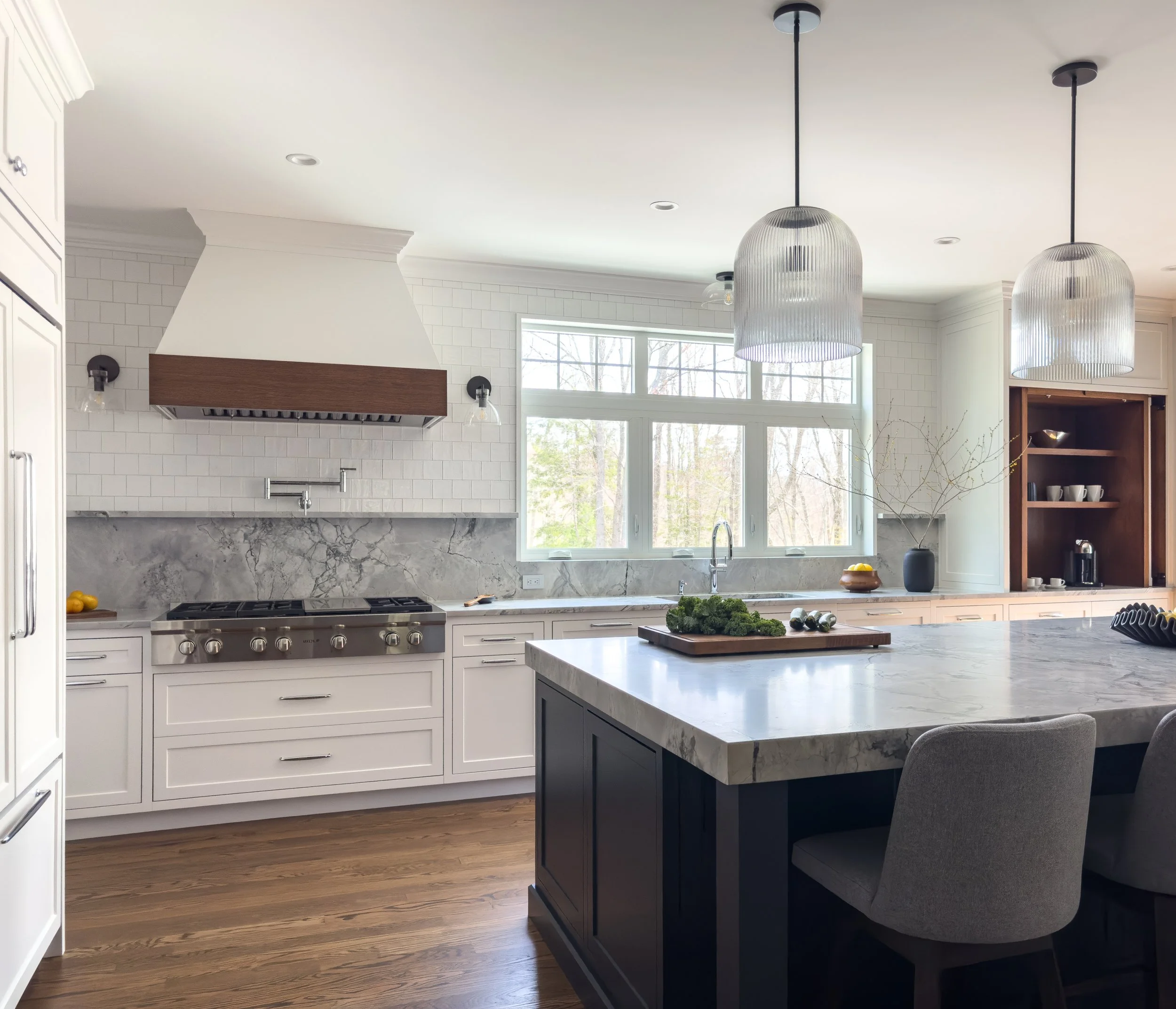 Renovated kitchen featuring white shaker cabinetry, a marble slab backsplash, walnut hood surround, and a dark island with stone countertop, designed by Tact & Grit Design Co.