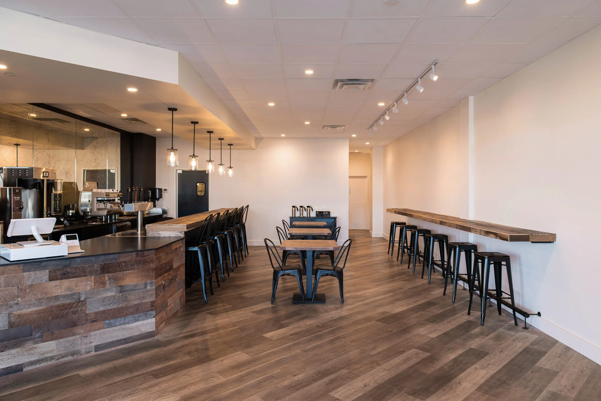 overall coffee shop fit out view featuring table and bar seating with warm wood, black granite countertops and fresh warm white walls
