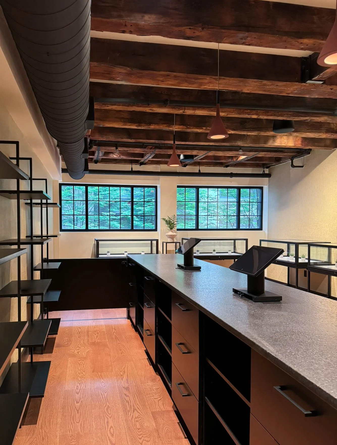 Completed commercial retail fit out in Boston featuring exposed timber ceiling beams, black granite counters at POS station, industrial windows, and display cases, designed by Tact & Grit Design Co.