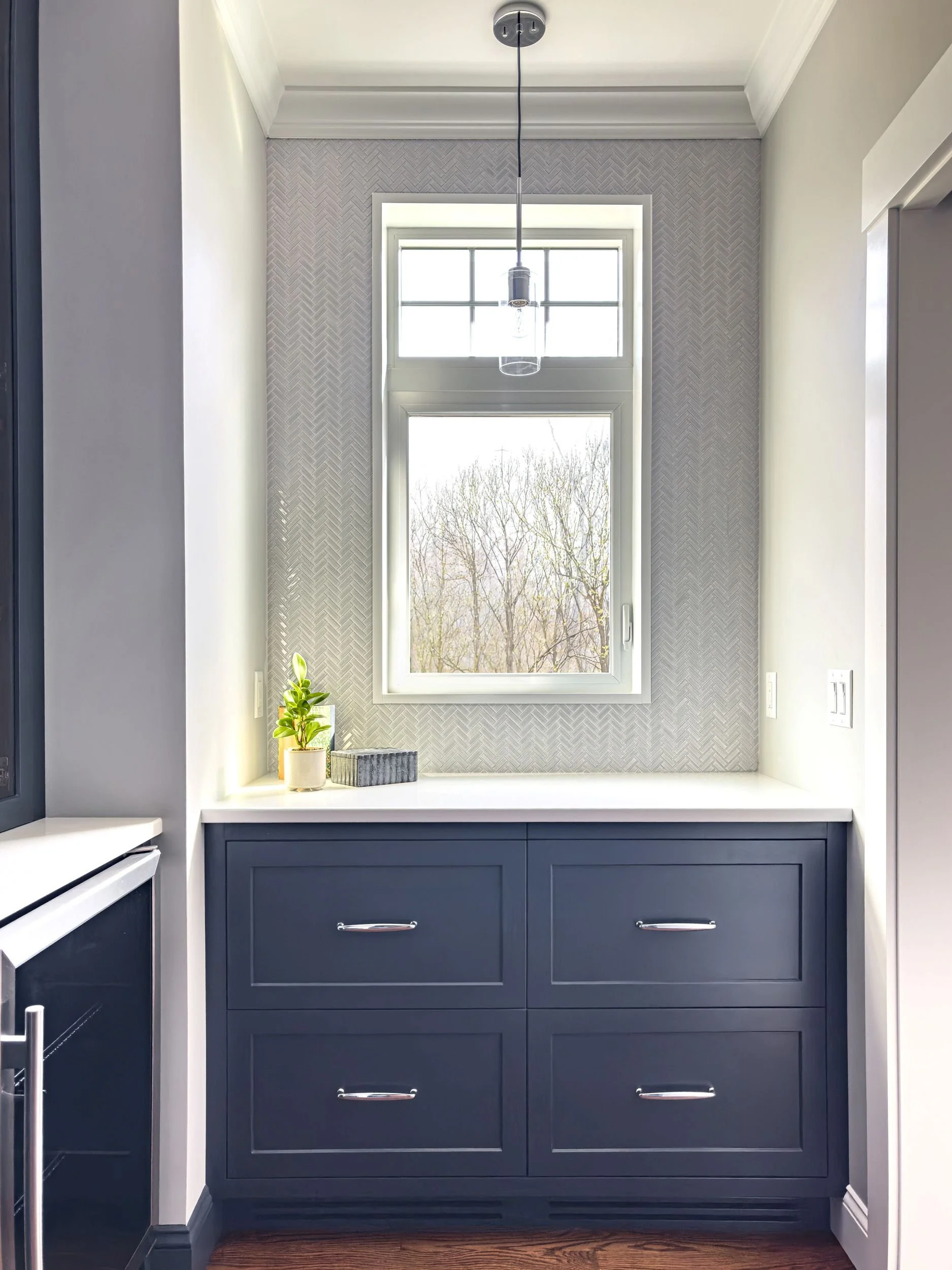 Slate blue butler's pantry with herringbone tile, pendant light, white quartz countertop, and natural light window in Hamilton MA home by Tact & Grit Design Co.
