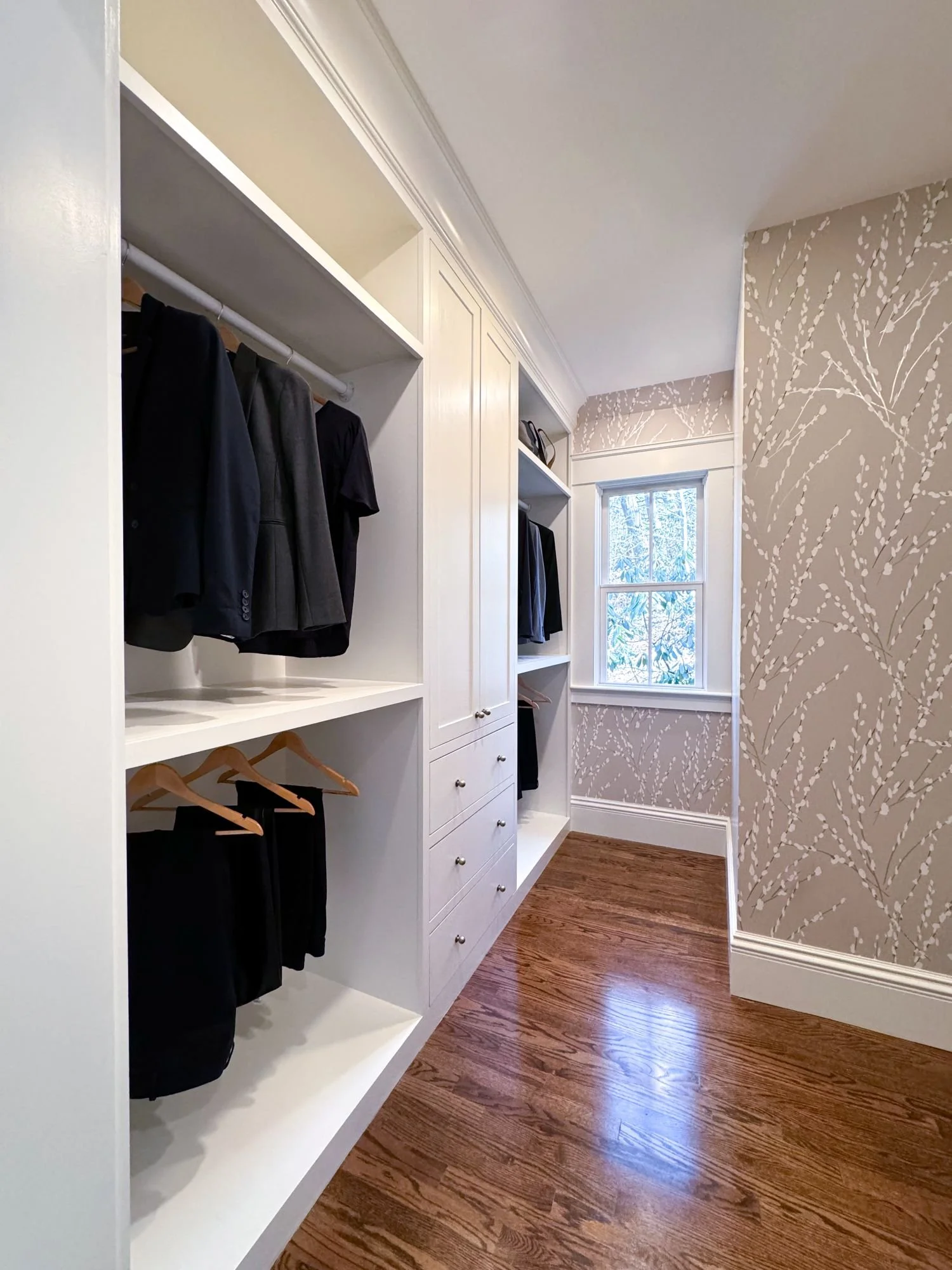 Renovated walk-in closet of an 1846 Victorian home in Newton MA featuring custom built-in hanging storage, shelving and drawers with decorative wallpaper