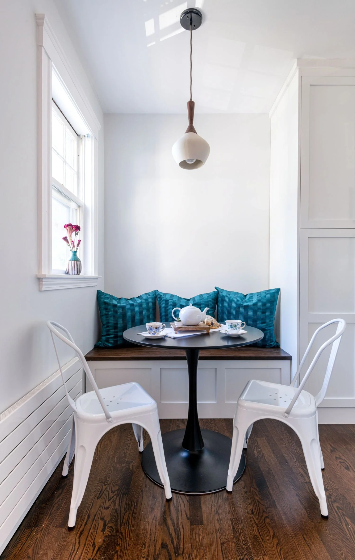 Breakfast nook in Medford, MA kitchen with two white chairs, a black table, pendant light and built-in bench