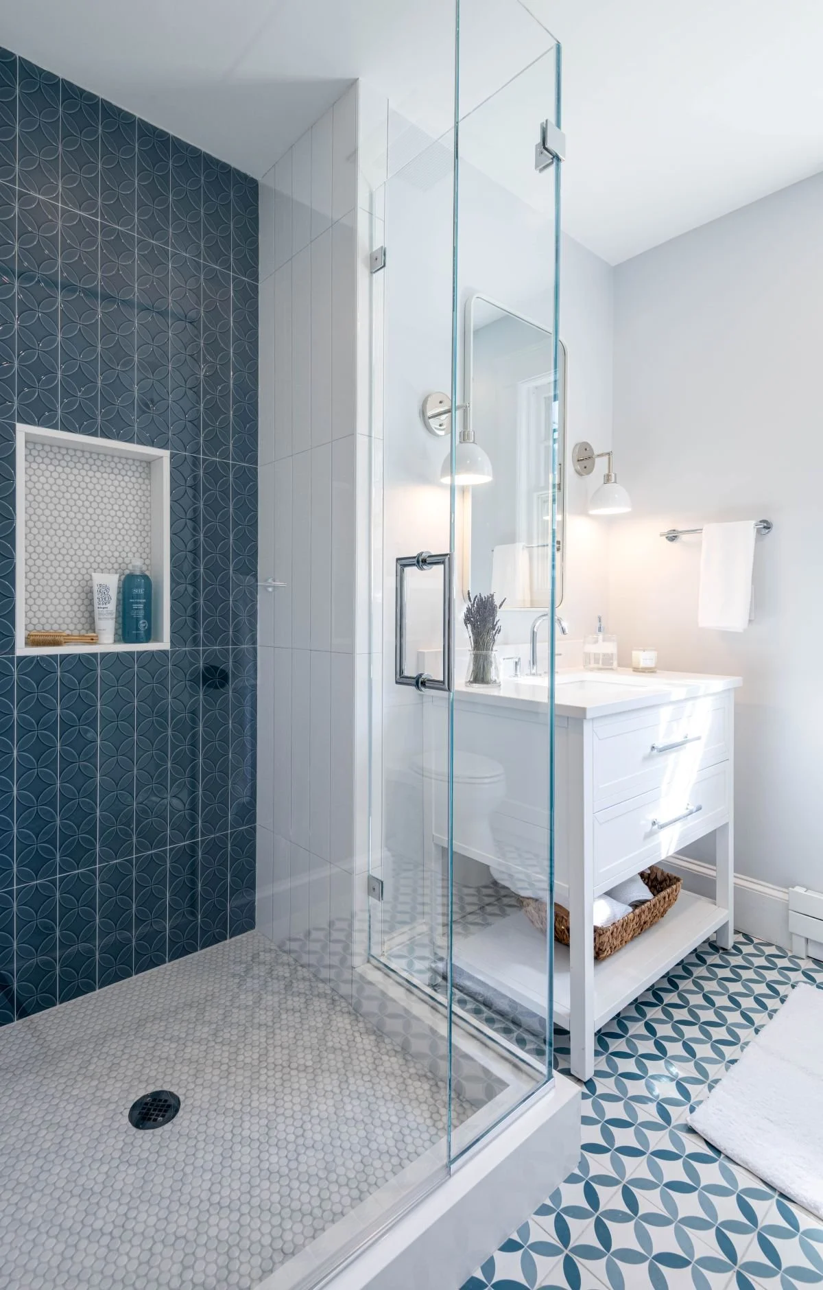 Completed secondary bathroom featuring a walk-in glass shower with blue patterned wall tiles, a white vanity, and geometric floor tile design.