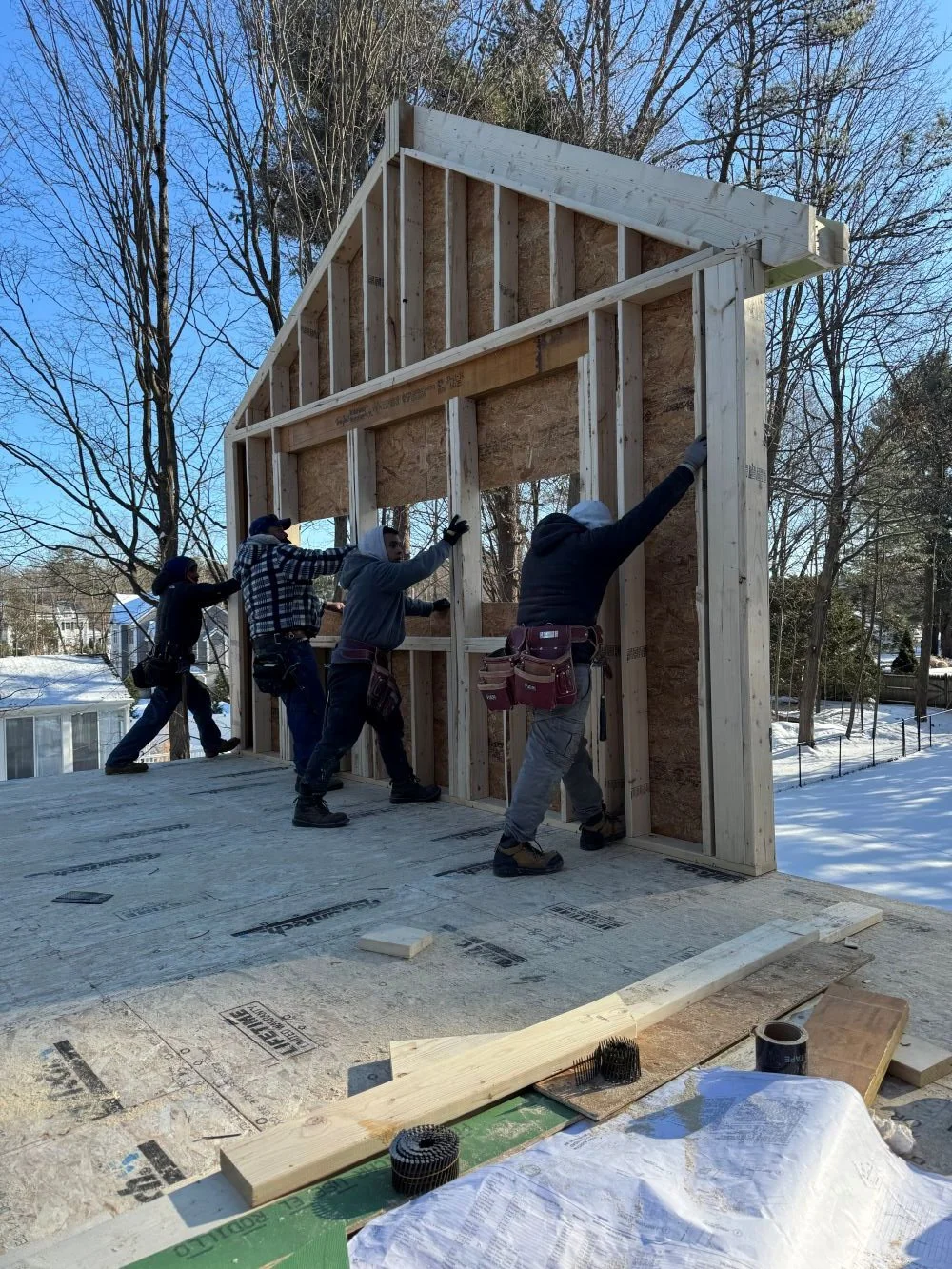 Second level exterior gable wall framing being tilted up in place by framing crew for a Dutch Colonial second story addition in Greater Boston designed by Tact and Grit Design Co.