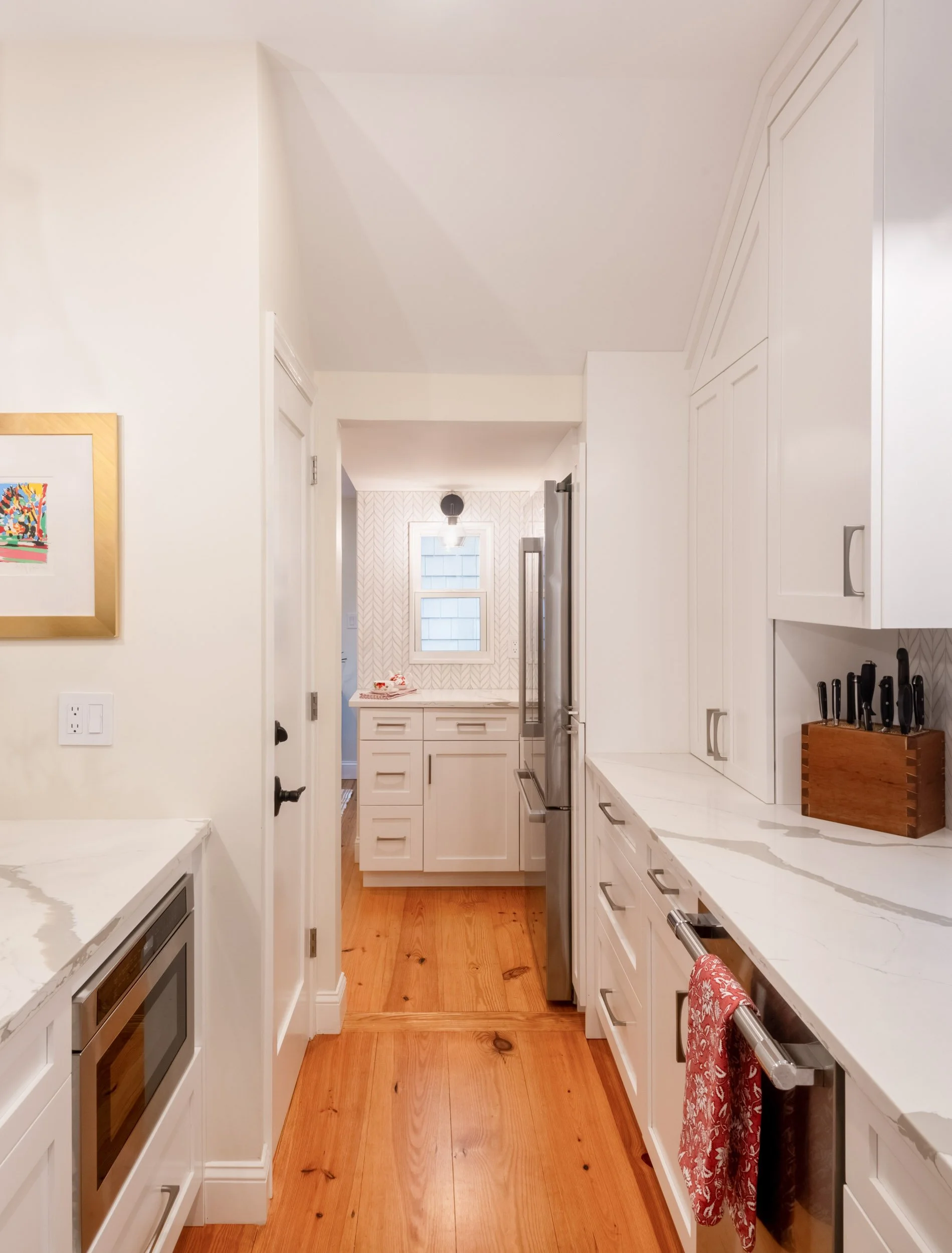A galley-style kitchen with white cabinetry and wide-plank pine floors.