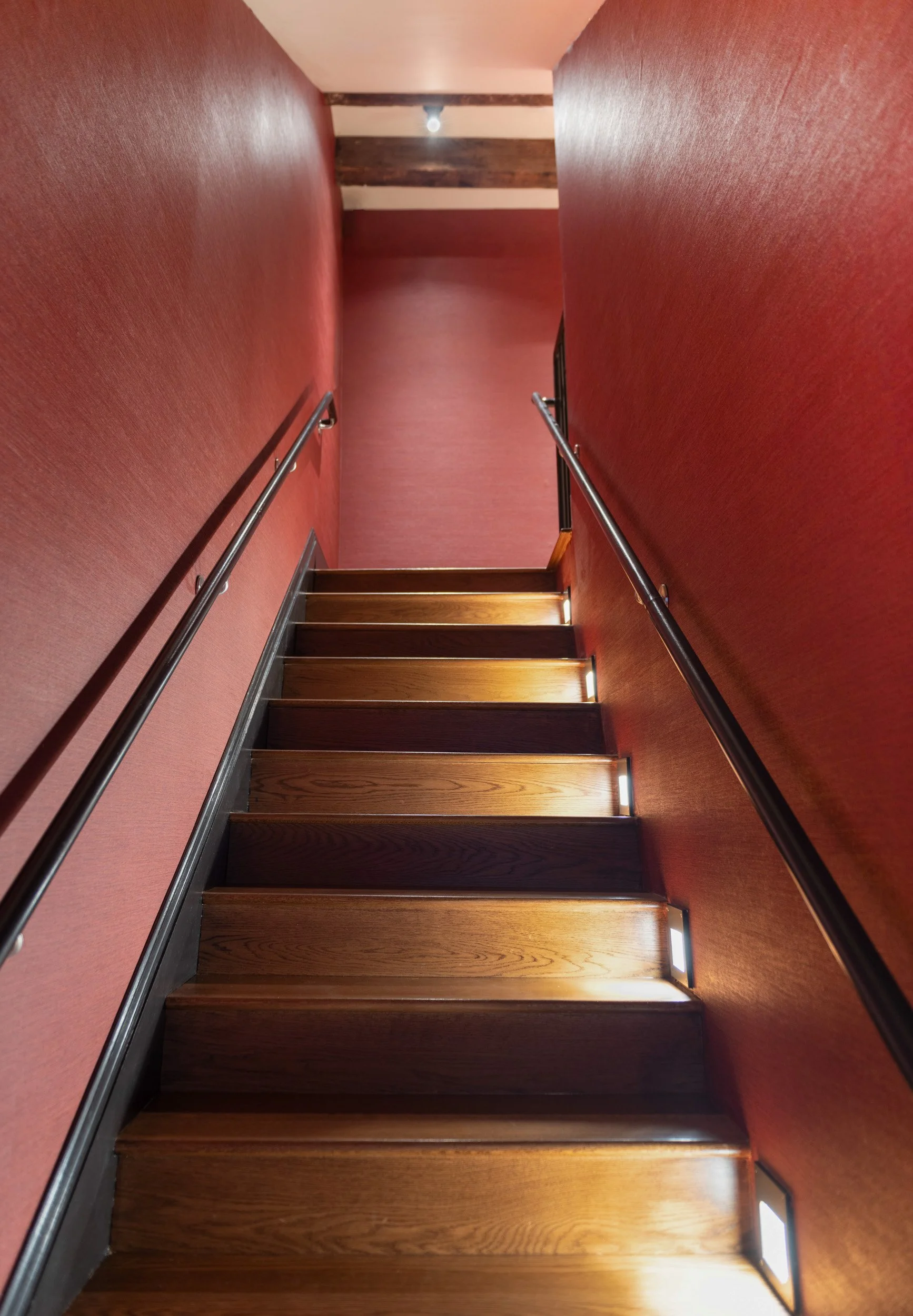 Main staircase featuring textured red wall covering, black railings and skirt board with step lights.