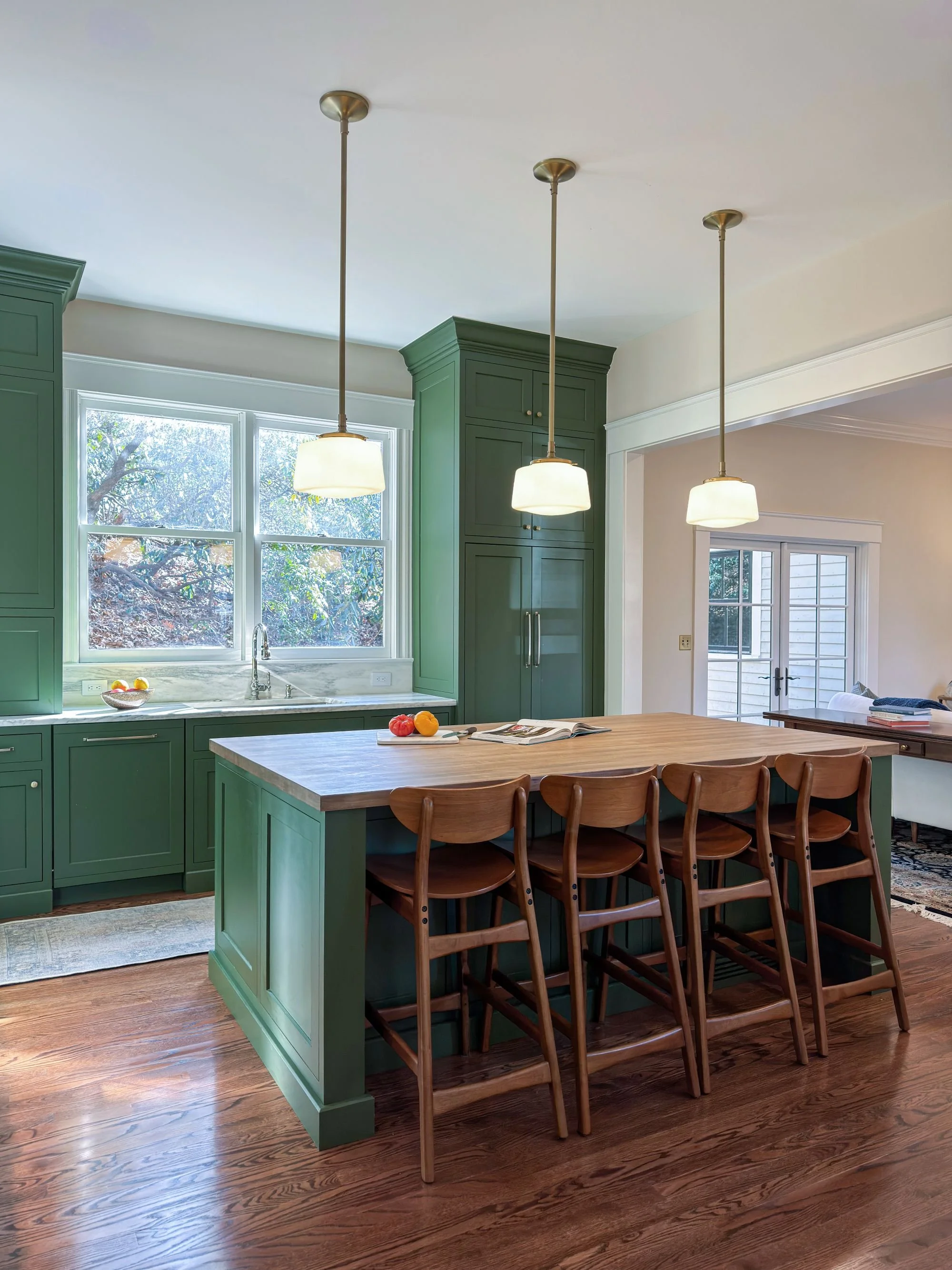 Renovated kitchen in an 1846 Victorian home in Newton MA showing view from island toward den with green cabinetry and pendant lighting