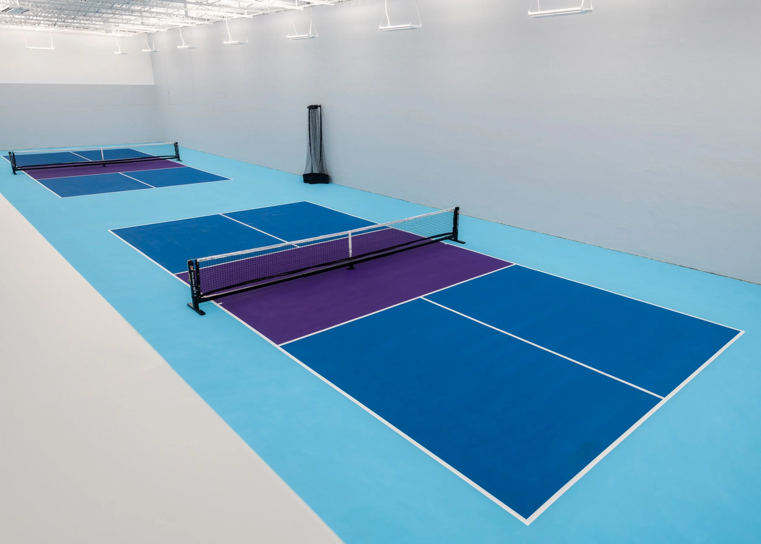 Two blue and purple pickleball courts from viewing area with high bay lighting
