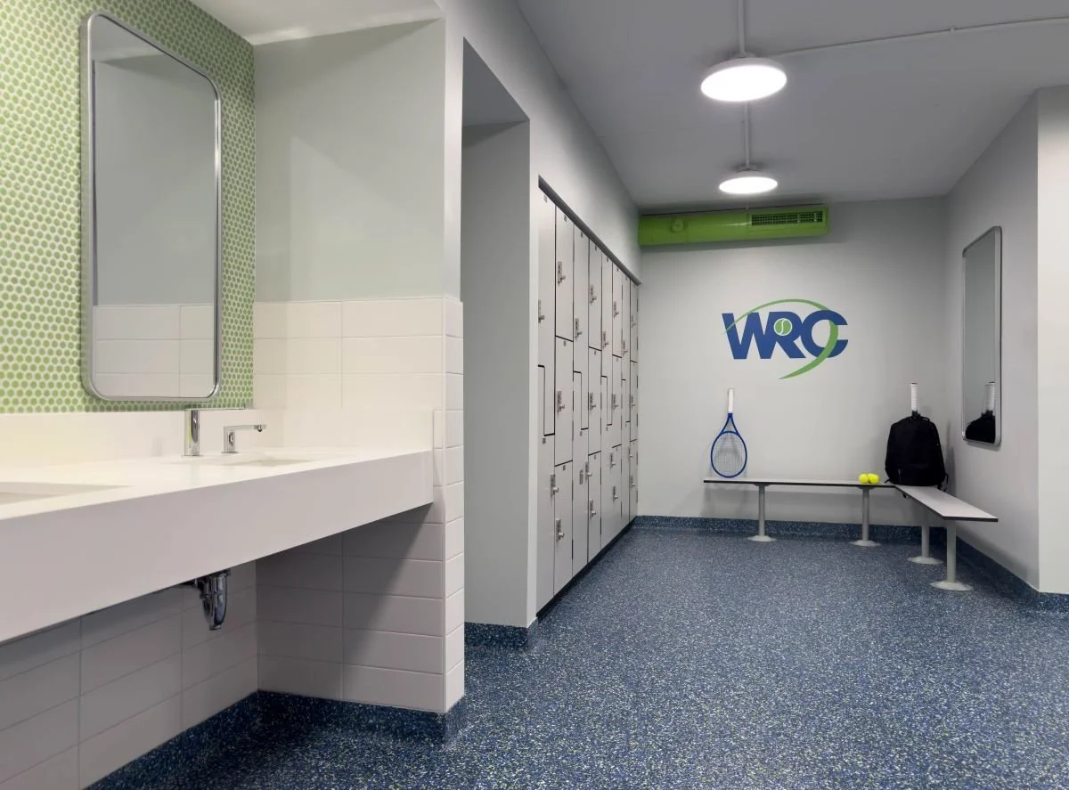 The completed locker room overhaul featuring clean architectural lines, integrated locker systems, custom vanity with green mosaic tile, and professional branding."