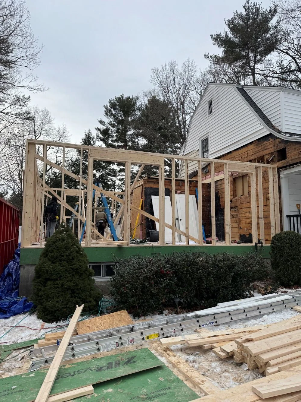 Ground level exterior framing phase of a Dutch Colonial second story addition in Greater Boston showing new wall framing and structural system designed by Tact and Grit Design Co.