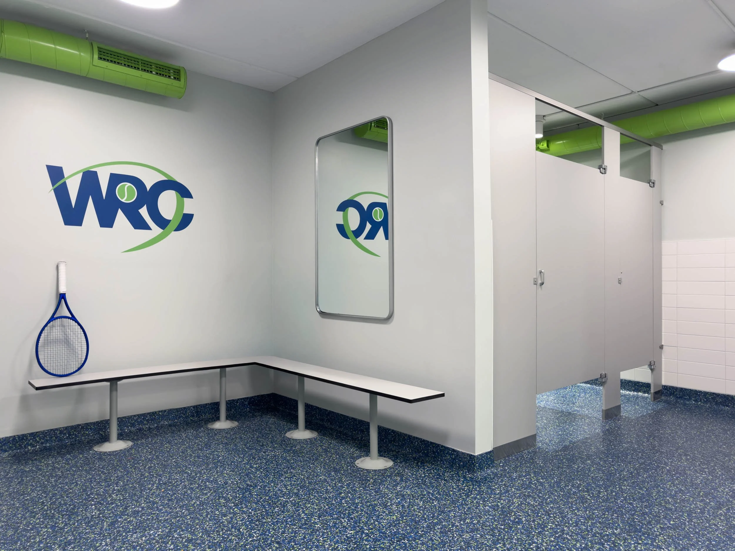 locker room changing area and toilet stalls with blue and green epoxy flooring and green exposed ductwork