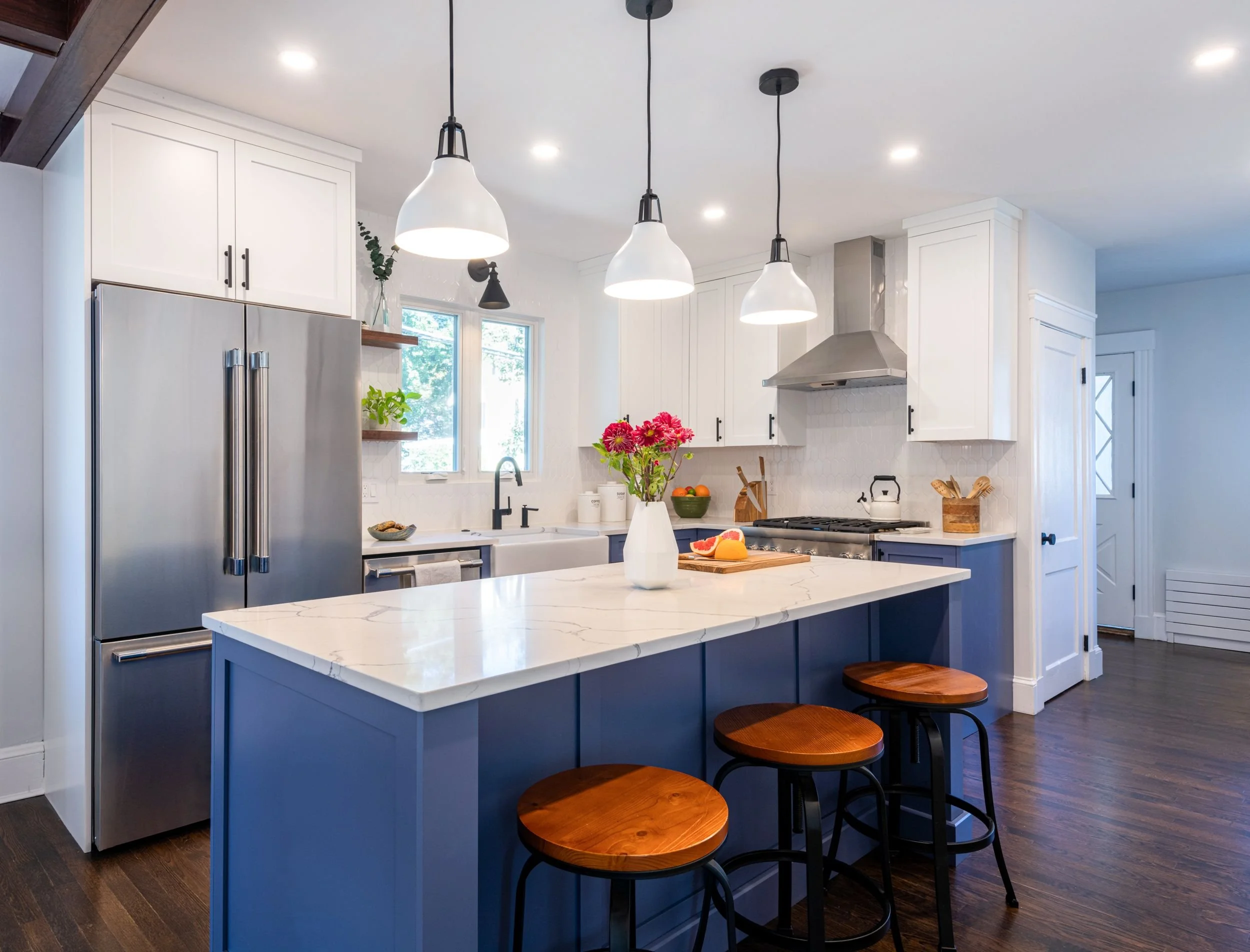 Periwinkle painted island with three bar stools facing refrigerator and sink wall in Medford, MA kitchen.