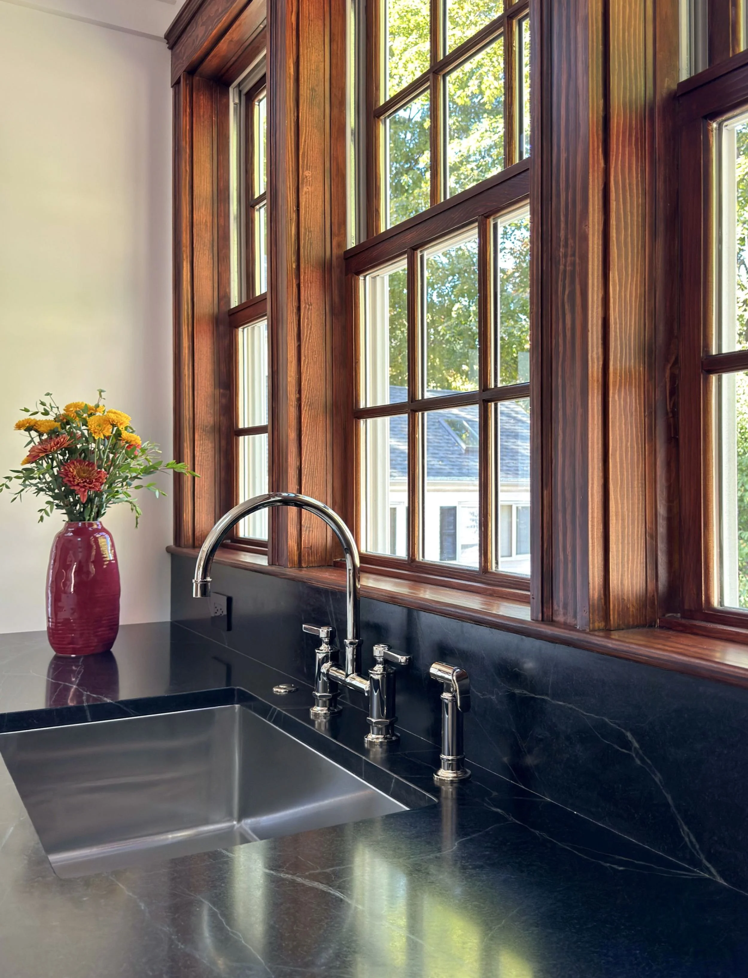 Soapstone countertops with stainless steel undermount sink with bridge faucet below dark-stained wood-framed windows, Medford MA kitchen addition