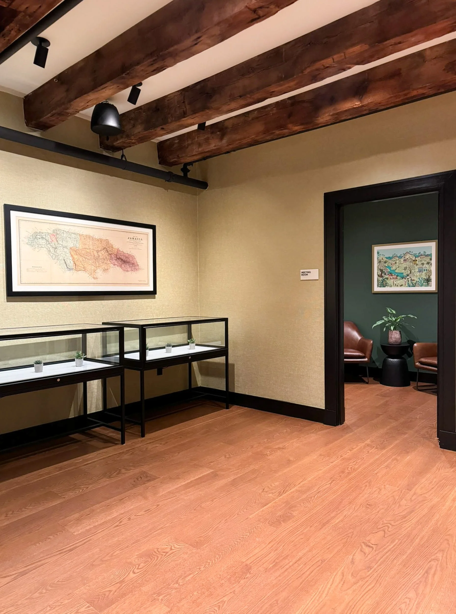 Glass displays with gold texture wall covering and a Jamaica map under original heavy timber beams with a private meeting room beyond.