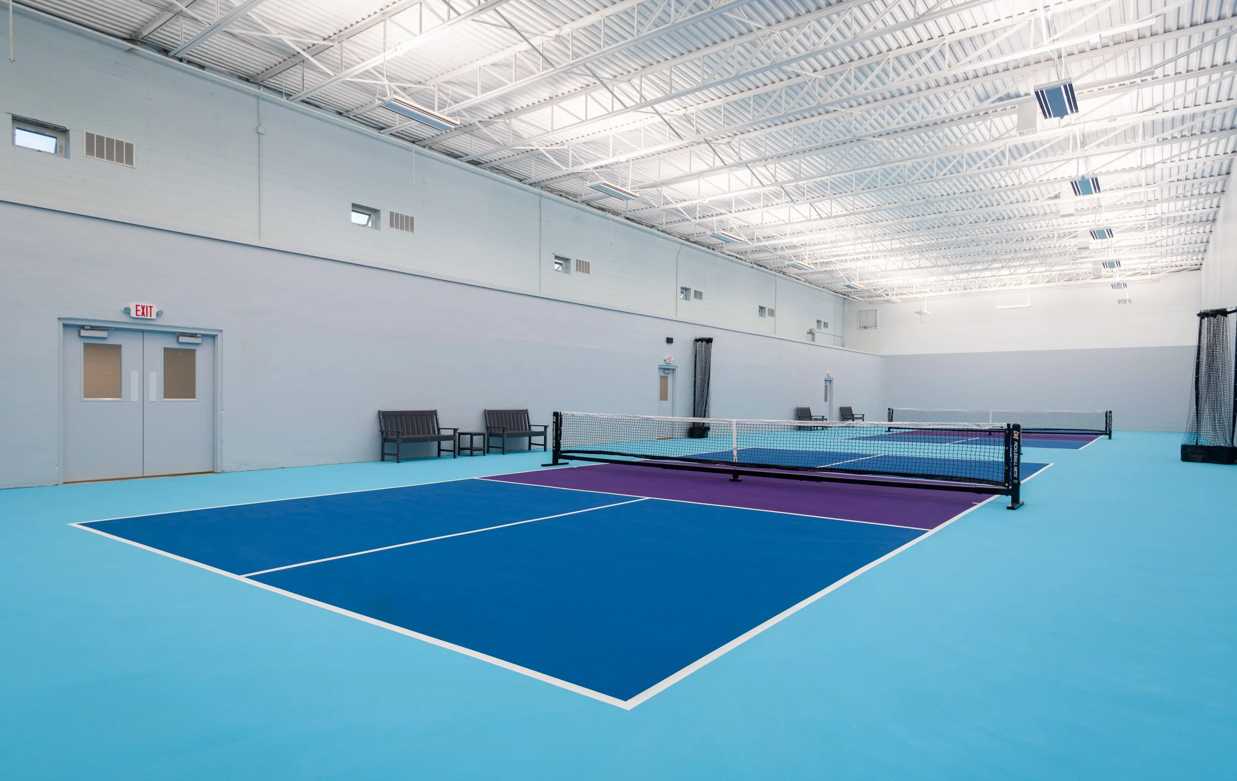overview of high bay space with exposed steel i-joists and two blue and purple pickleball courts with viewing above.