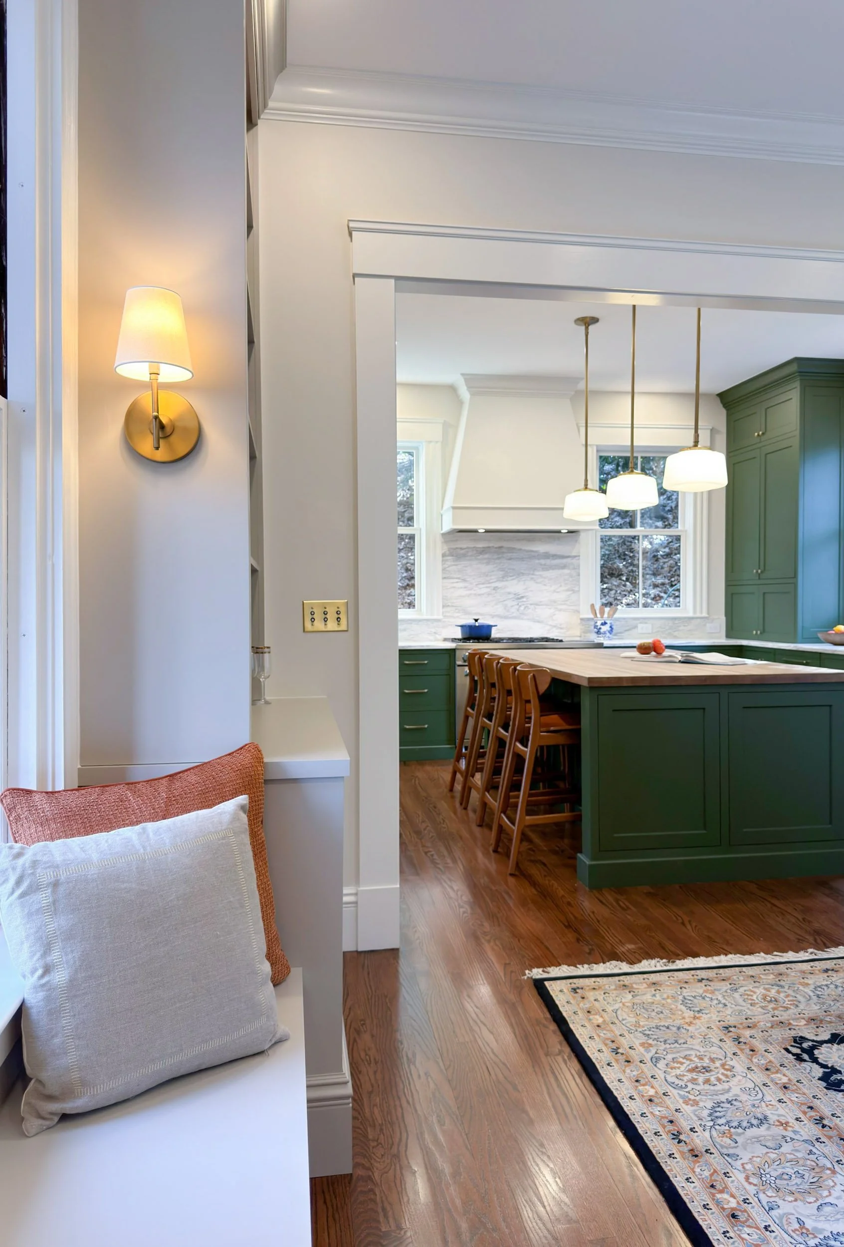 View from new den built-ins featuring a reading bench into the kitchen of an 1846 Victorian home in Newton MA with green cabinetry beyond