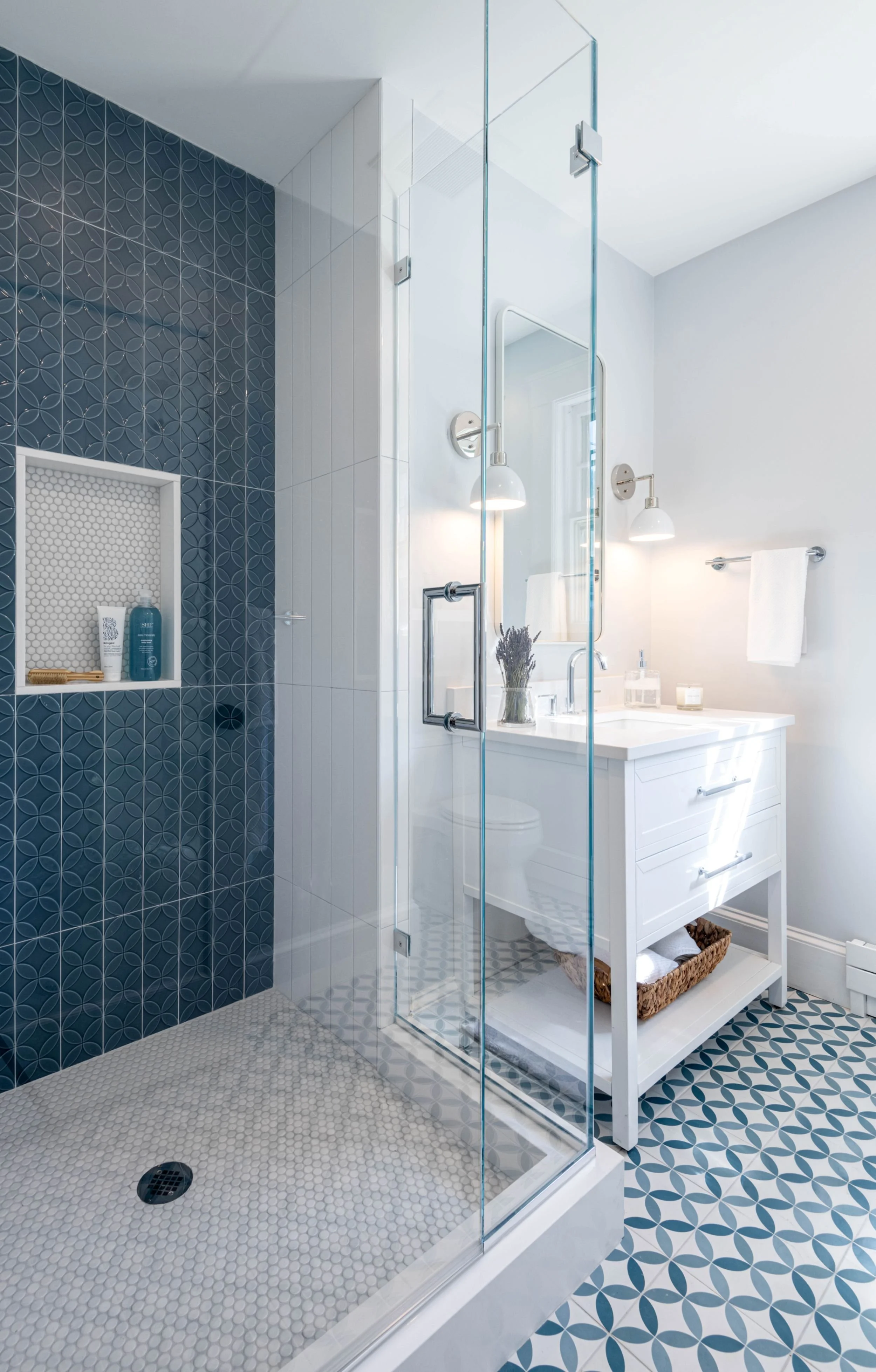 completed secondary bathroom remodel featuring a walk-in-shower with modern vertical blue and white tile, penny mosaic floor and white vanity with sconces