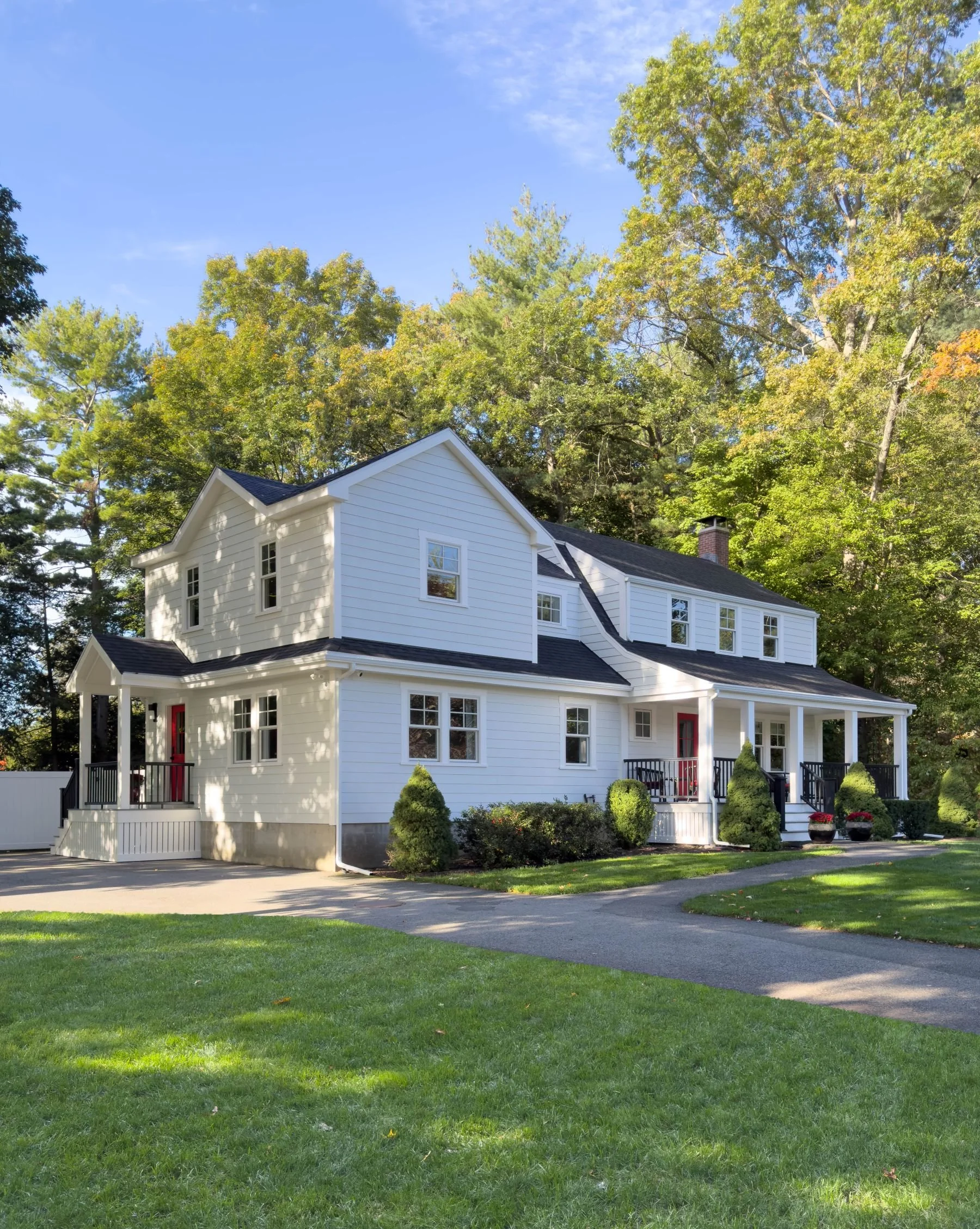 Completed side angle view of a Dutch Colonial second story addition in Greater Boston showing new Hardie siding, Marvin windows, covered front porch and second story massing by Tact and Grit Design Co.