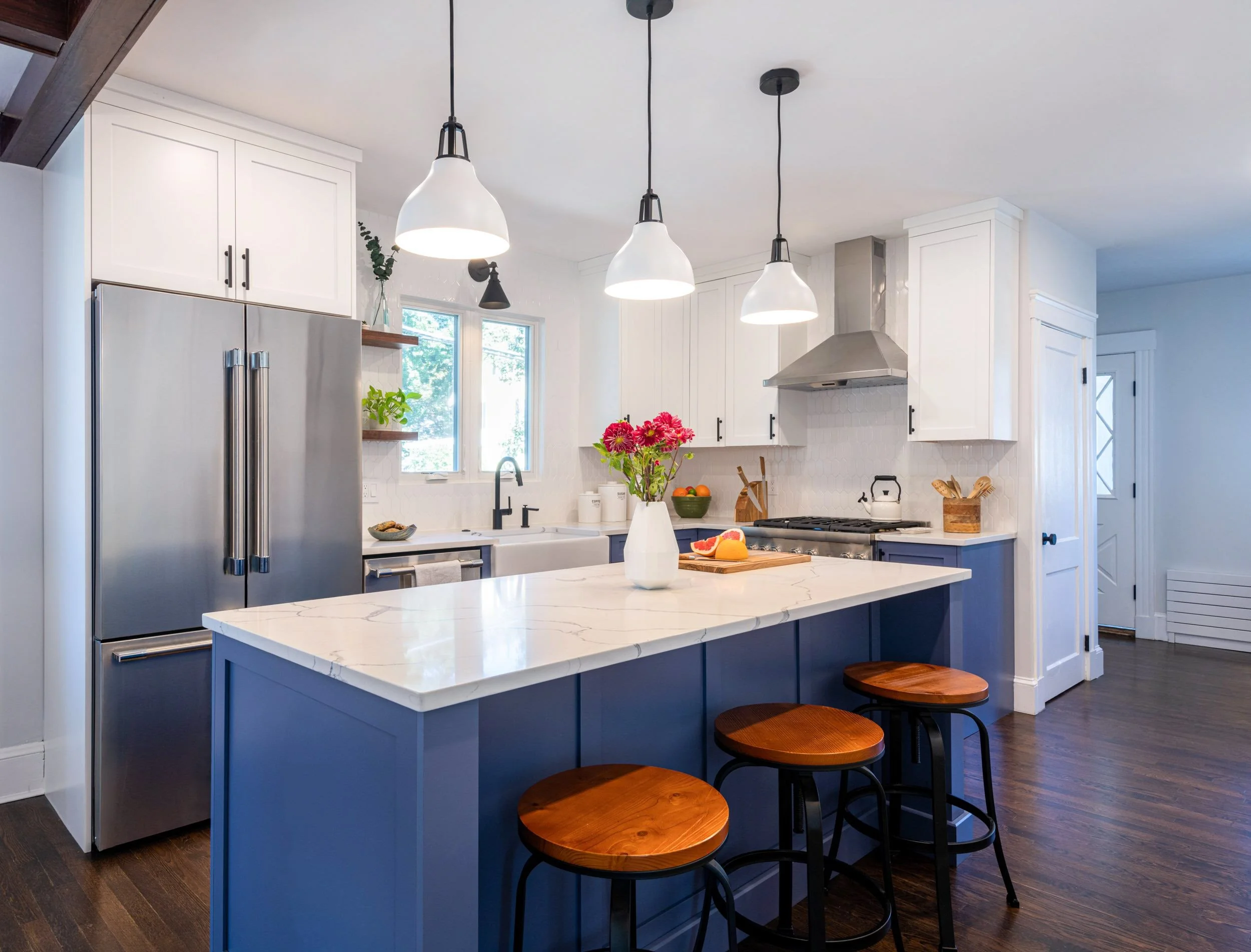 Periwinkle painted island with three bar stools facing refrigerator and sink wall in Medford, MA kitchen.