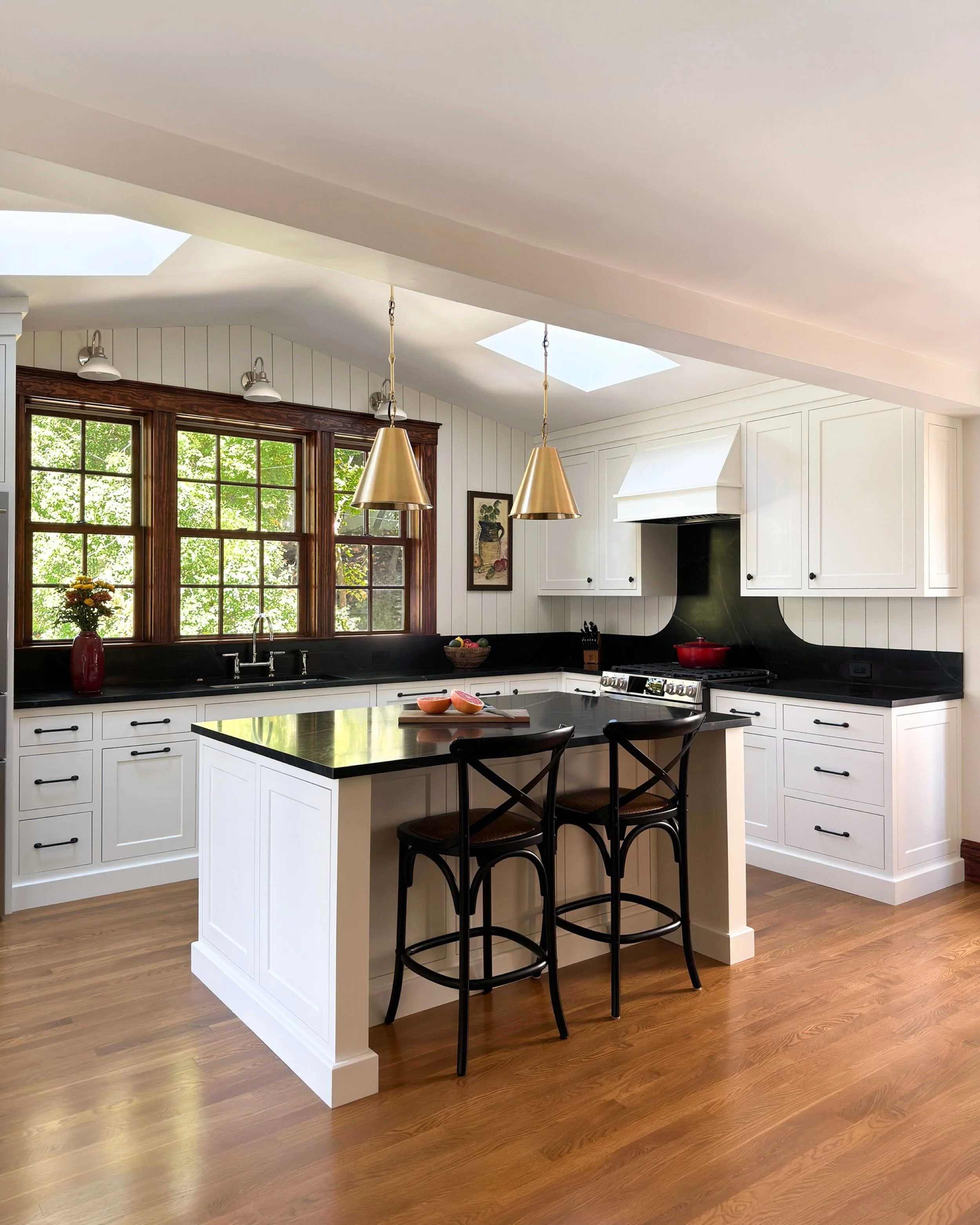 Overview of interior kitchen addition with soapstone countertops, white inset custom cabinetry and a triple window with stained casing in a Medford, MA home