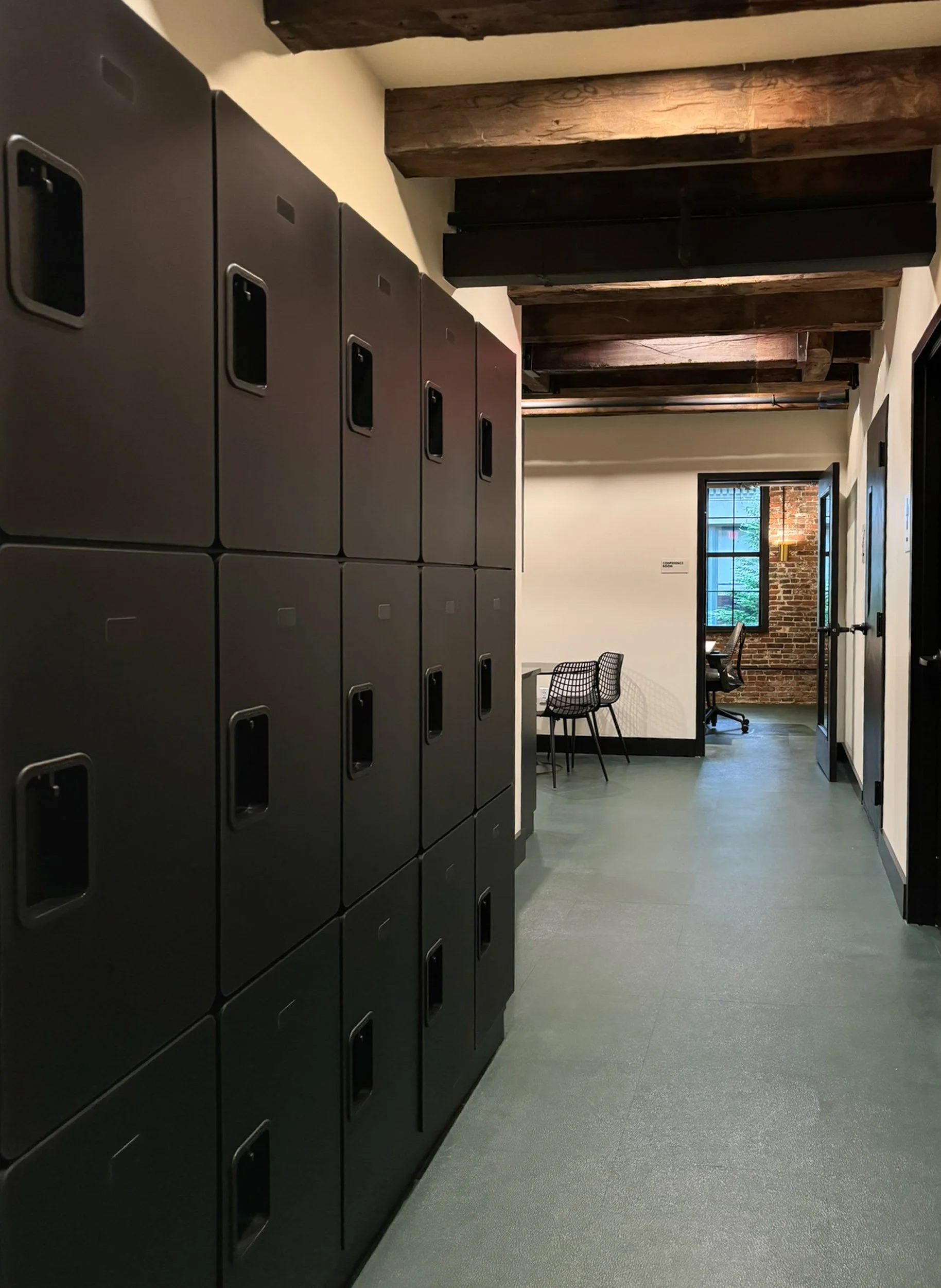 A hallway lined with black employee lockers beneath exposed wood beams in a converted downtown Boston commercial space.